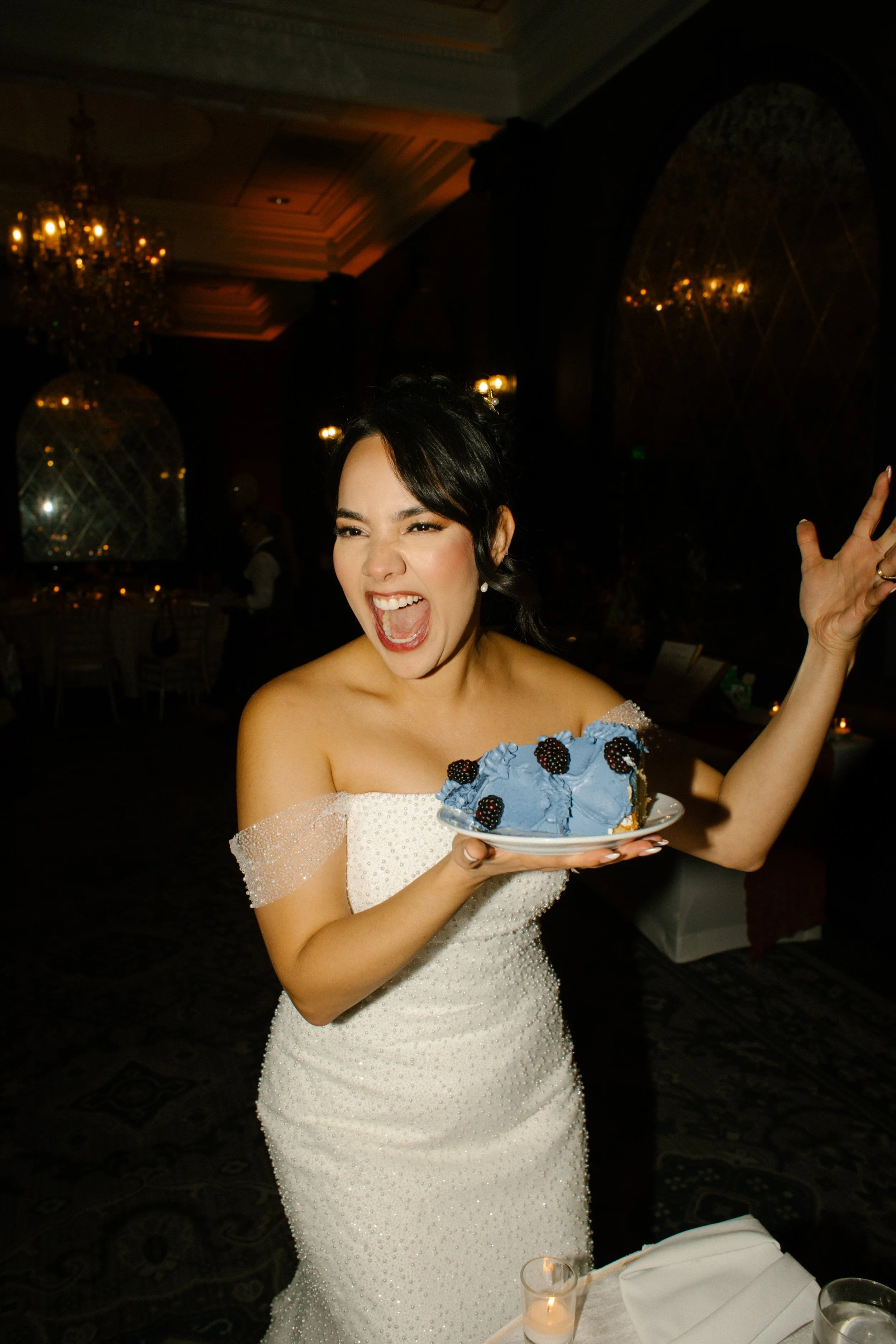 Bride holding a slice of blue wedding cake and celebrating with guests during the reception