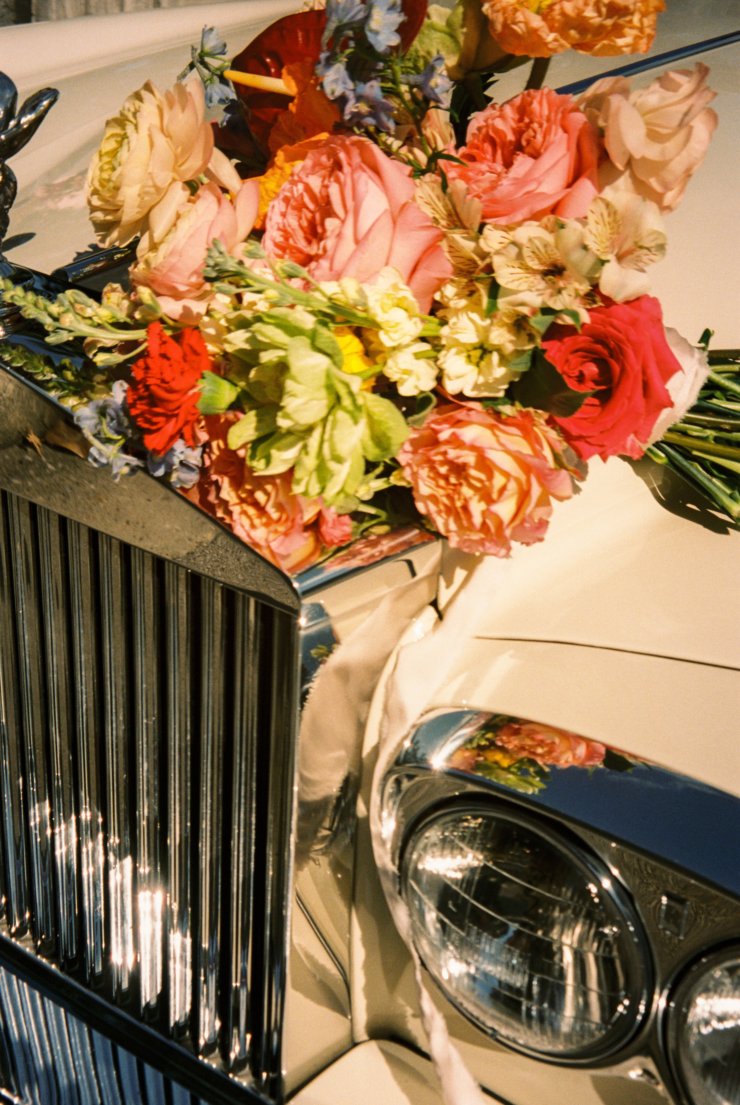Colorful bridal bouquet resting on a vintage luxury car hood, inspired by 2027 wedding trends