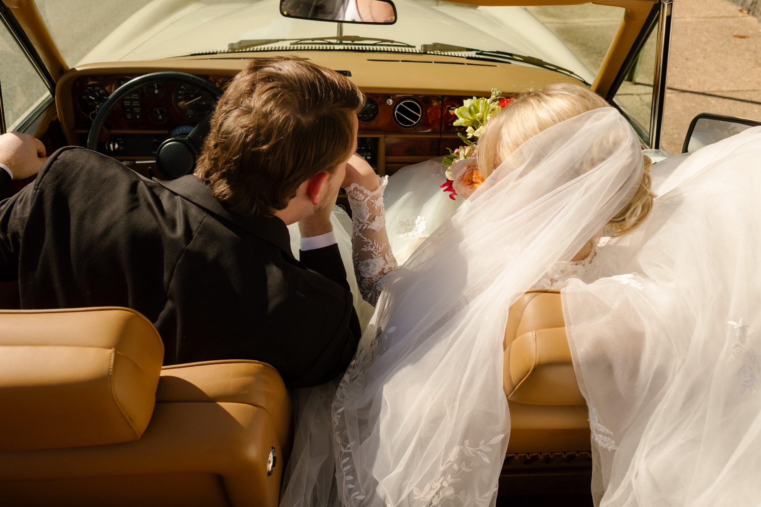 Newlyweds relaxing together inside a vintage convertible after their wedding ceremony