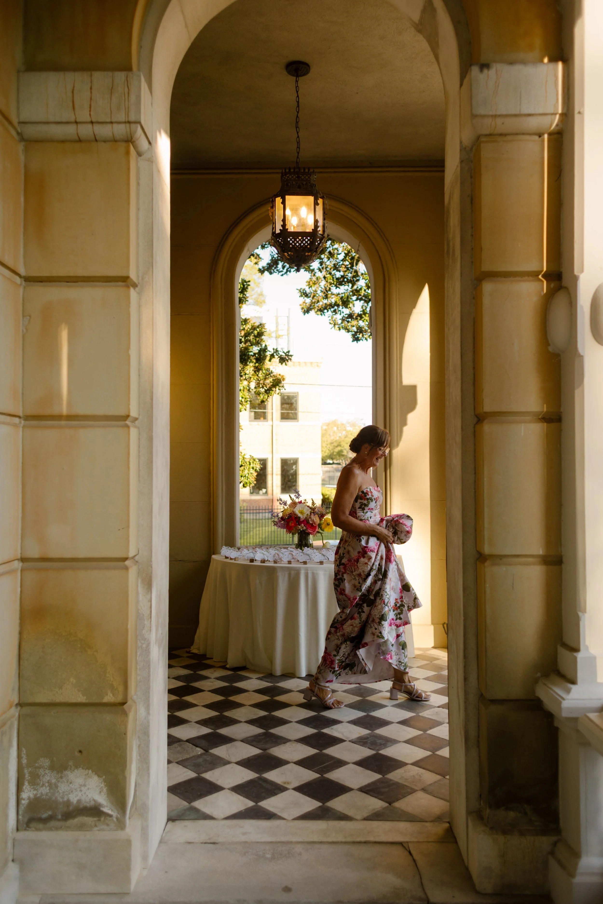 Wedding guest walking through a historic colonnade carrying a floral-patterned clutch
