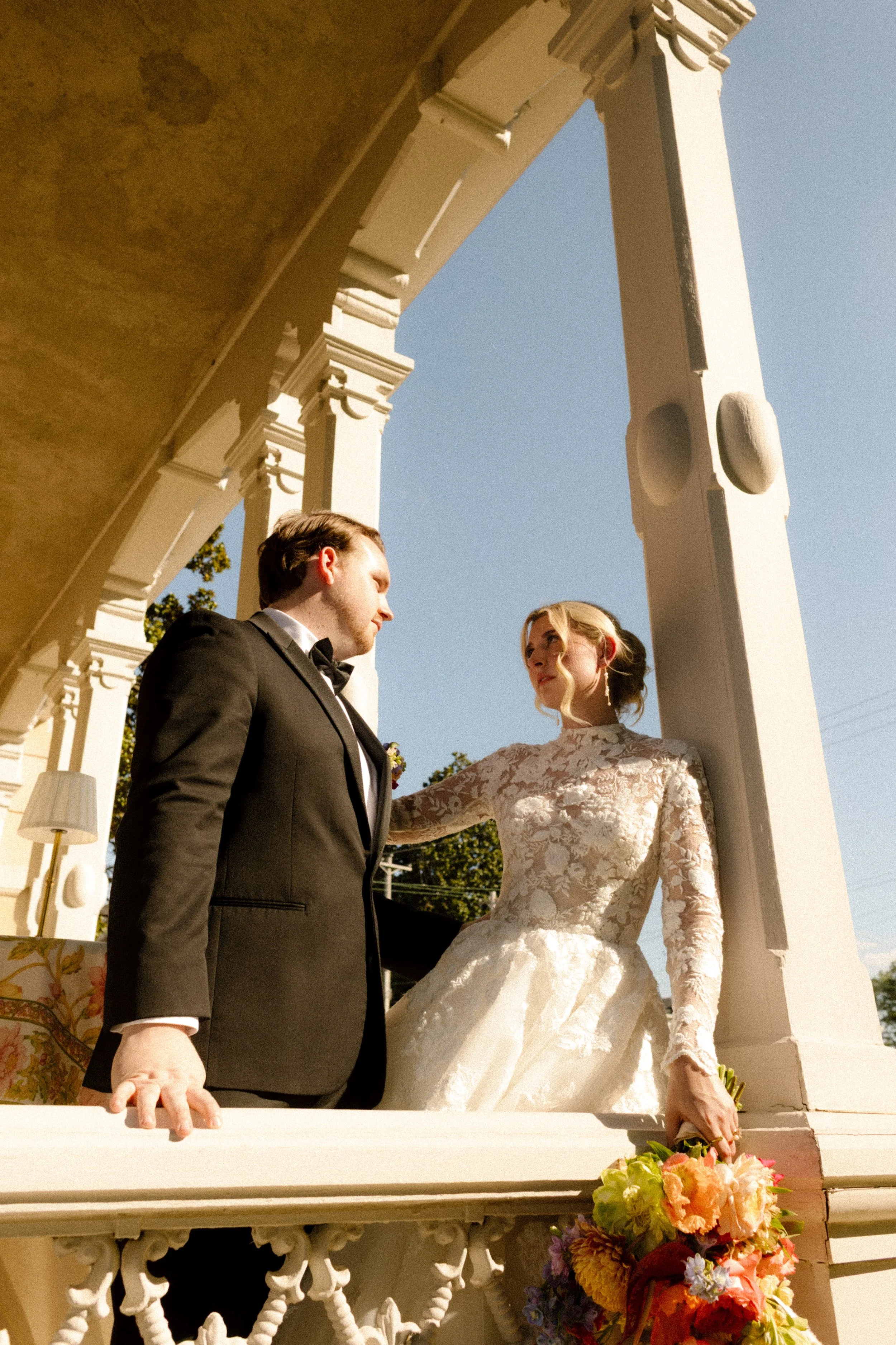 Bride and groom sharing a portrait on the veranda of a historic estate with vibrant florals and romantic architecture