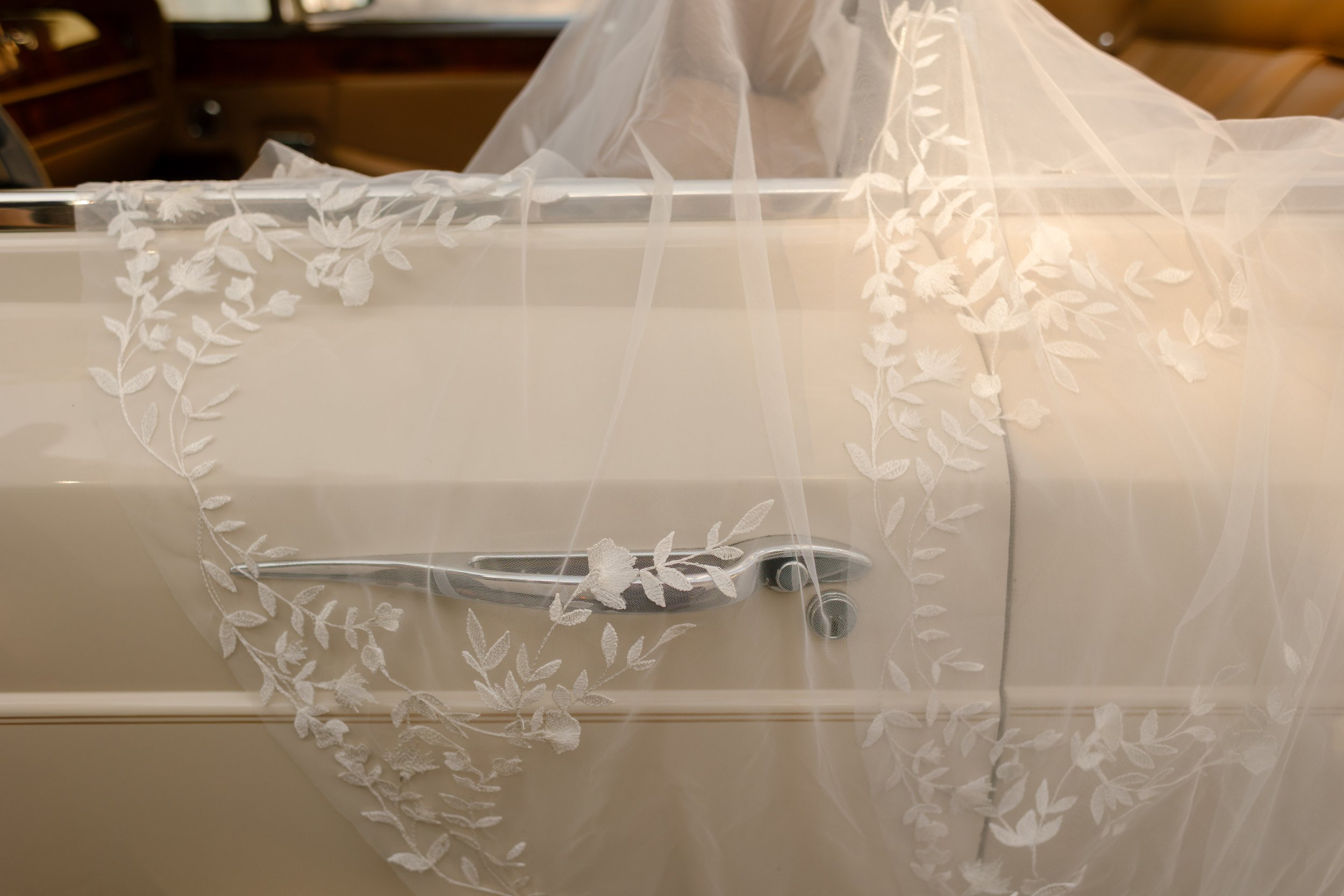 Embroidered wedding veil draped across the door of a vintage convertible, reflecting personalized details popular in 2027 wedding trends