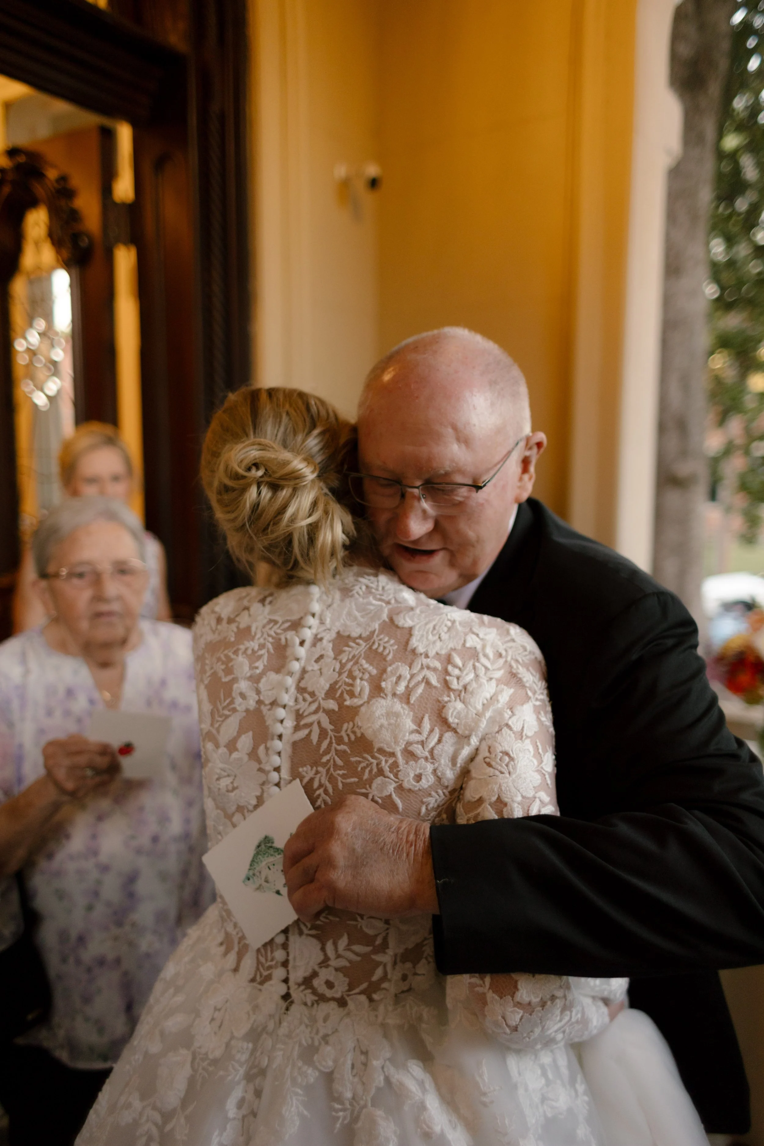 Bride sharing an emotional embrace with a family member before the ceremony while guests look on nearby