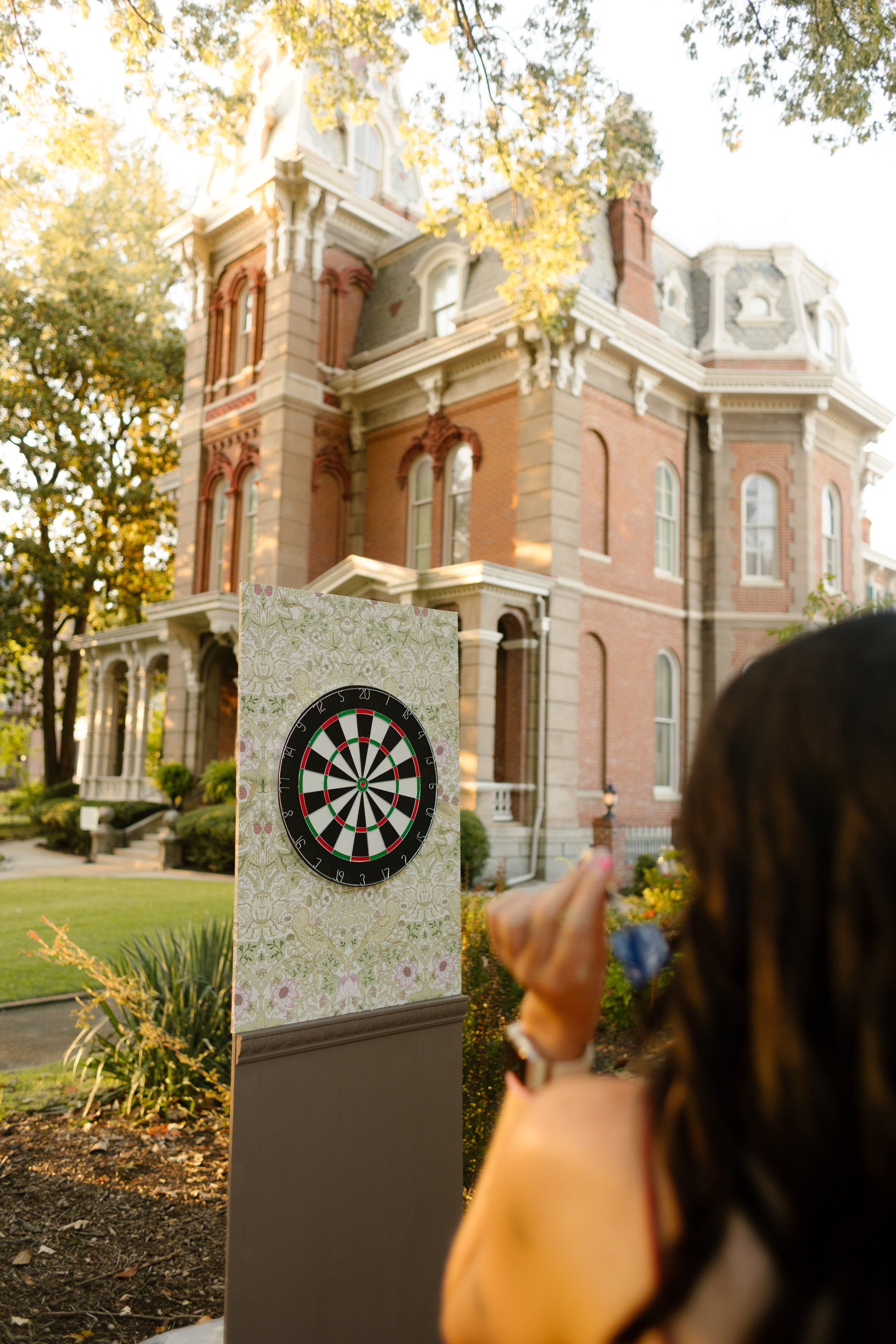 Wedding guest aiming a dart at a decorative dartboard station during a creative outdoor reception activity