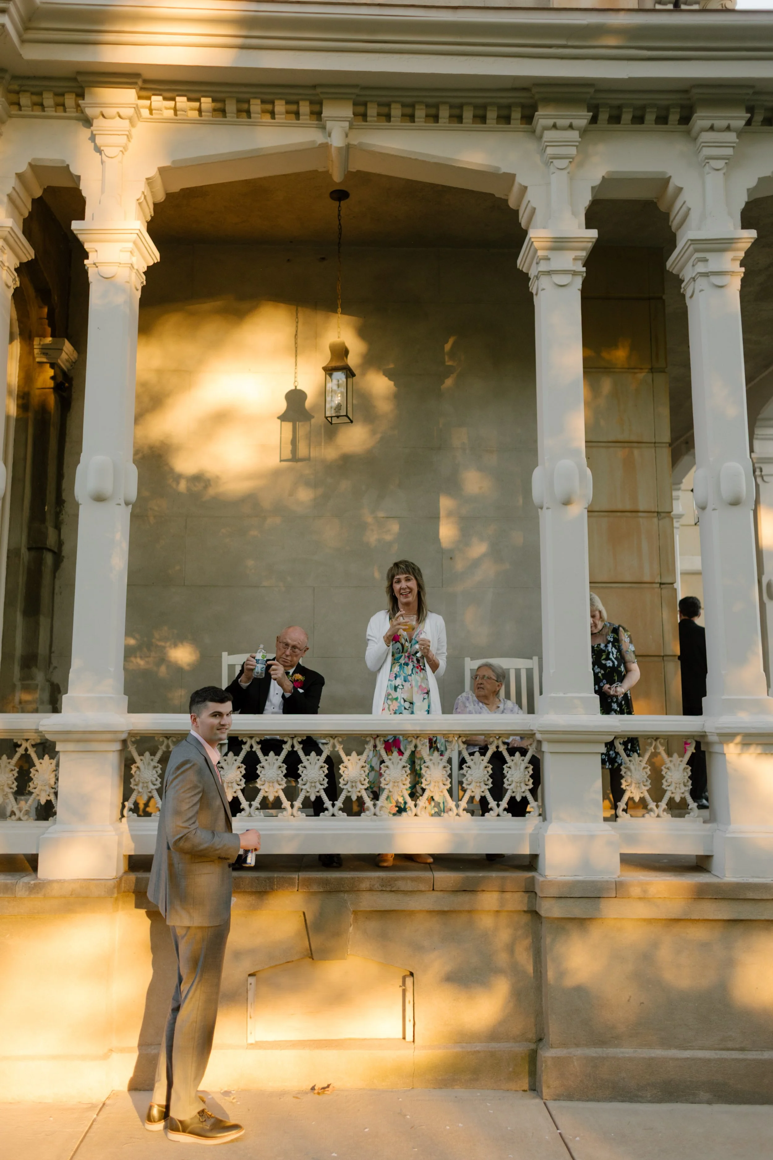 Family members gathered on the historic mansion porch watching wedding festivities during golden hour celebrations