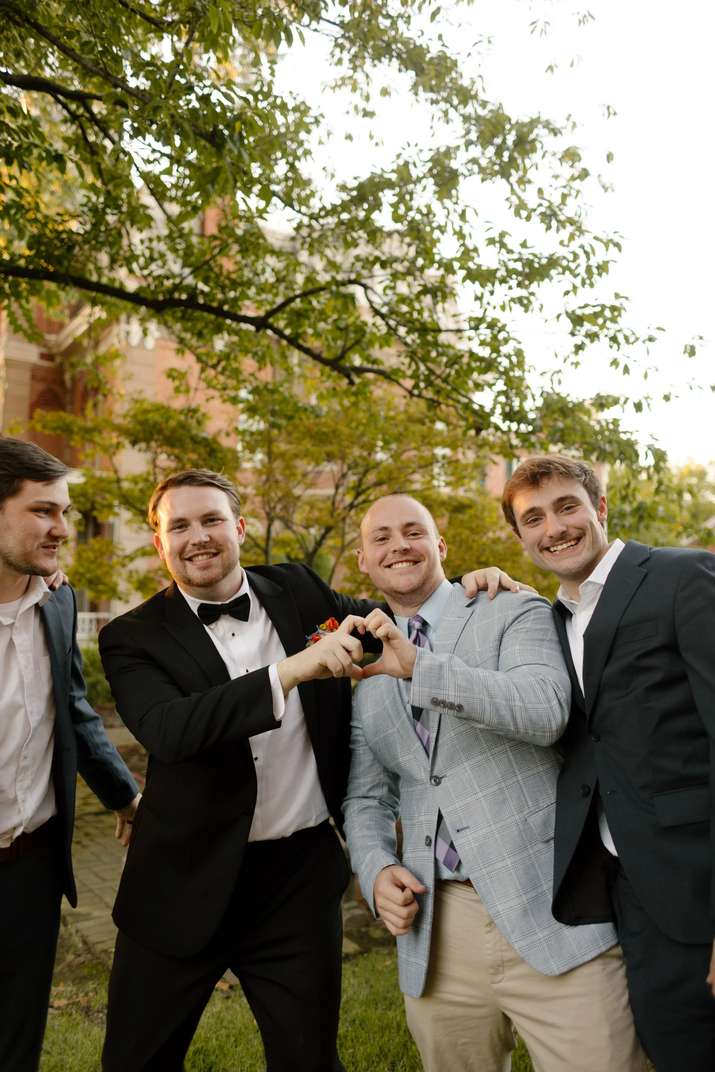 Groom posing with friends outdoors before the ceremony, capturing candid wedding party moments beneath historic estate trees