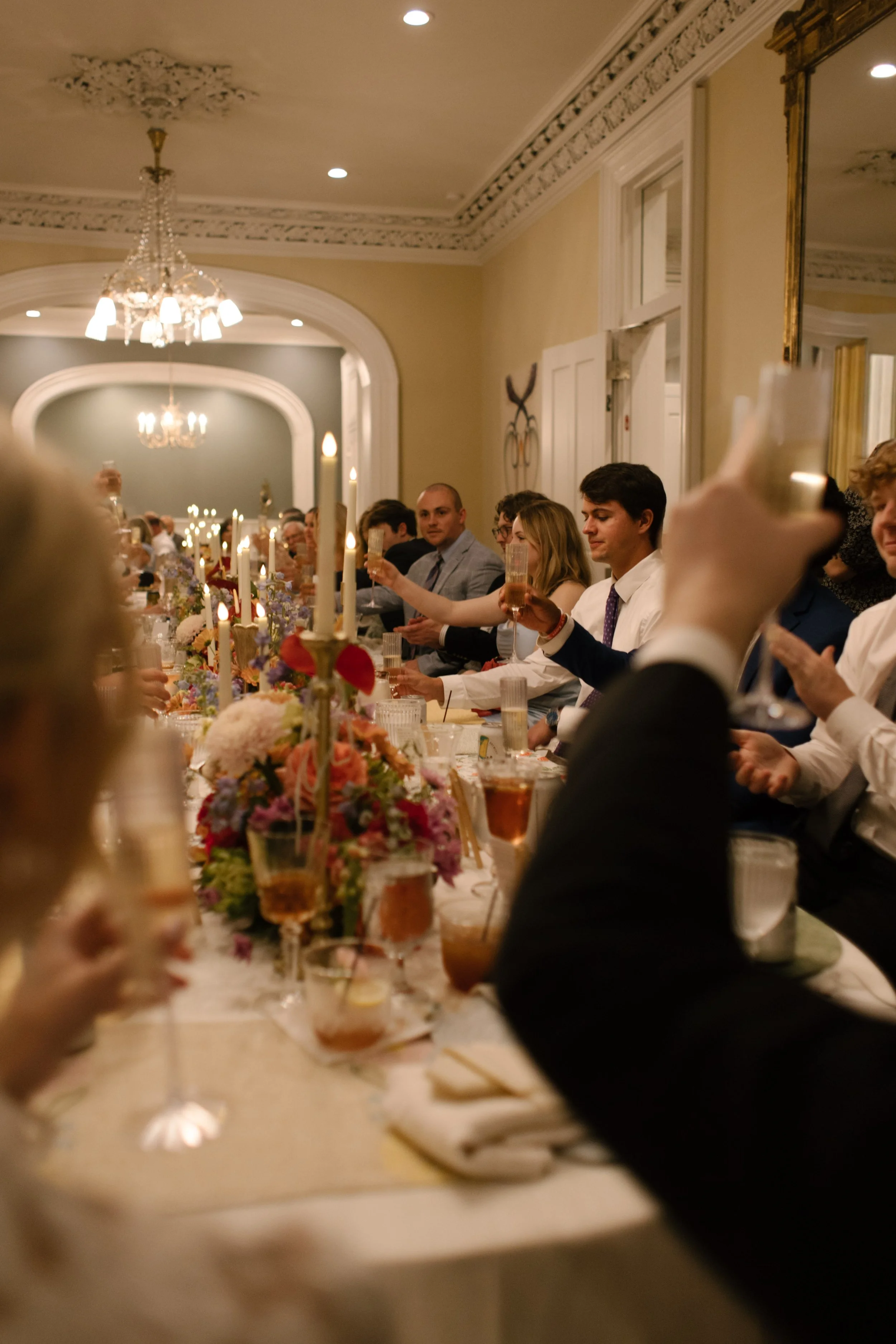 Family and friends raising champagne glasses for a celebratory wedding toast beneath sparkling chandeliers