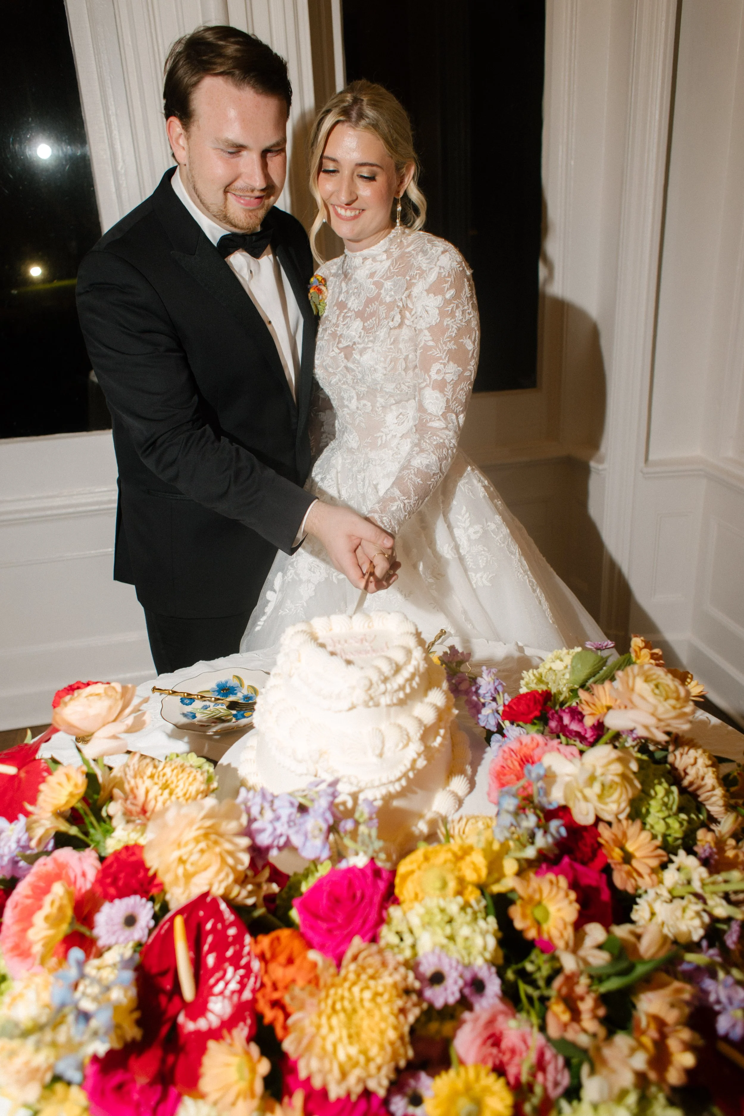 Bride and groom cutting their wedding cake surrounded by vibrant floral arrangements and romantic reception decor