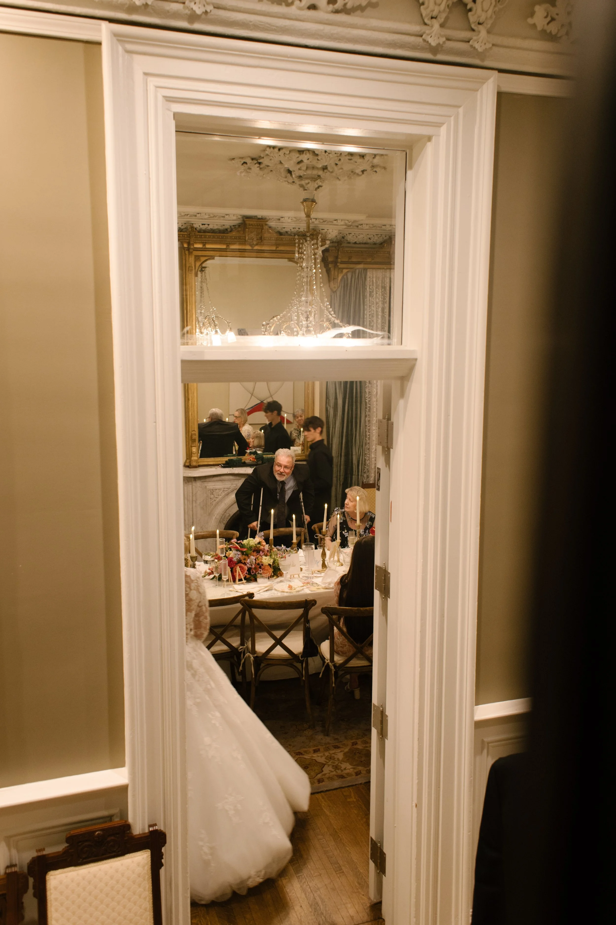 A candid glimpse through the doorway capturing guests gathered around a beautifully decorated reception table