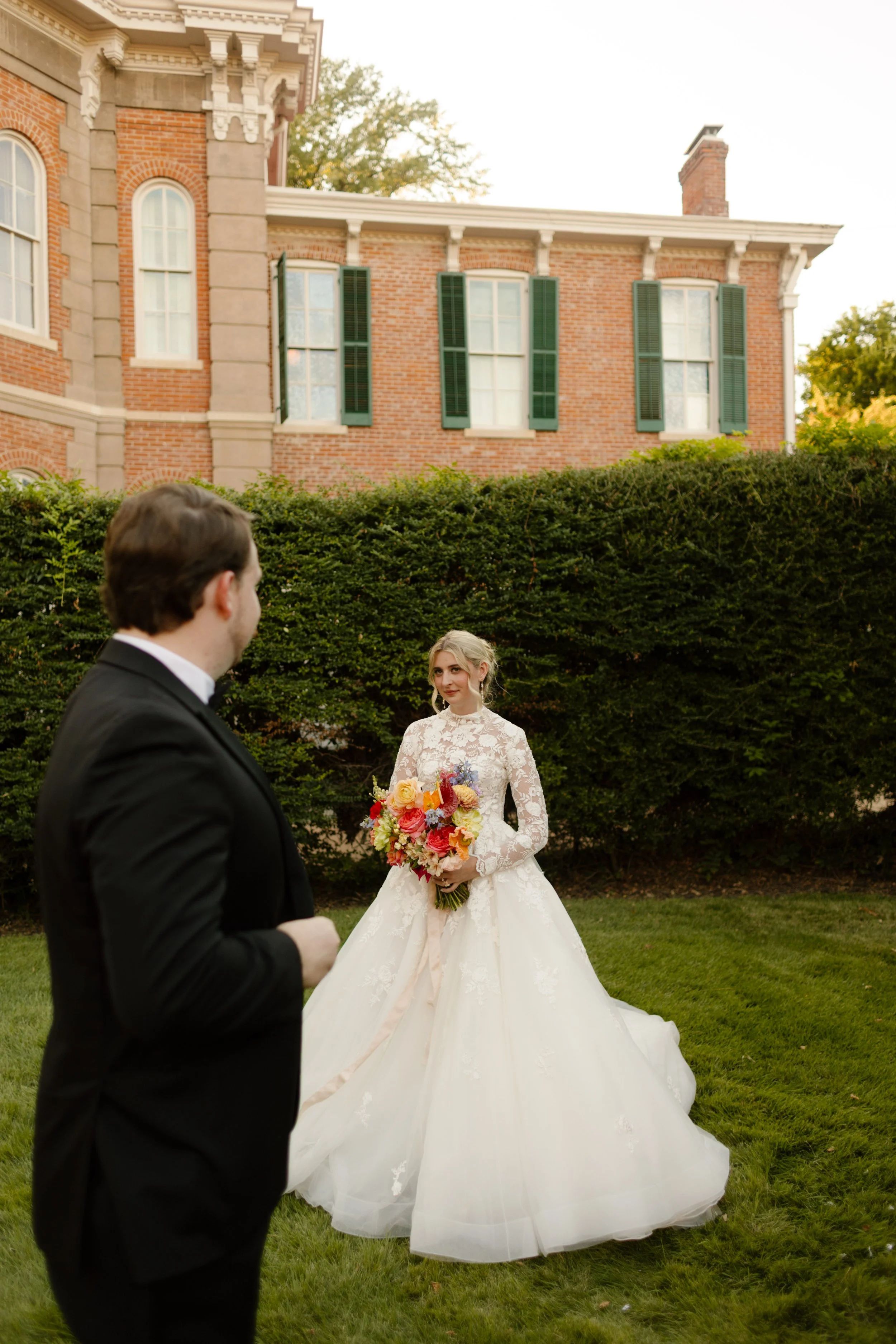 The groom admiring his bride as she stands in the garden holding her colorful bouquet