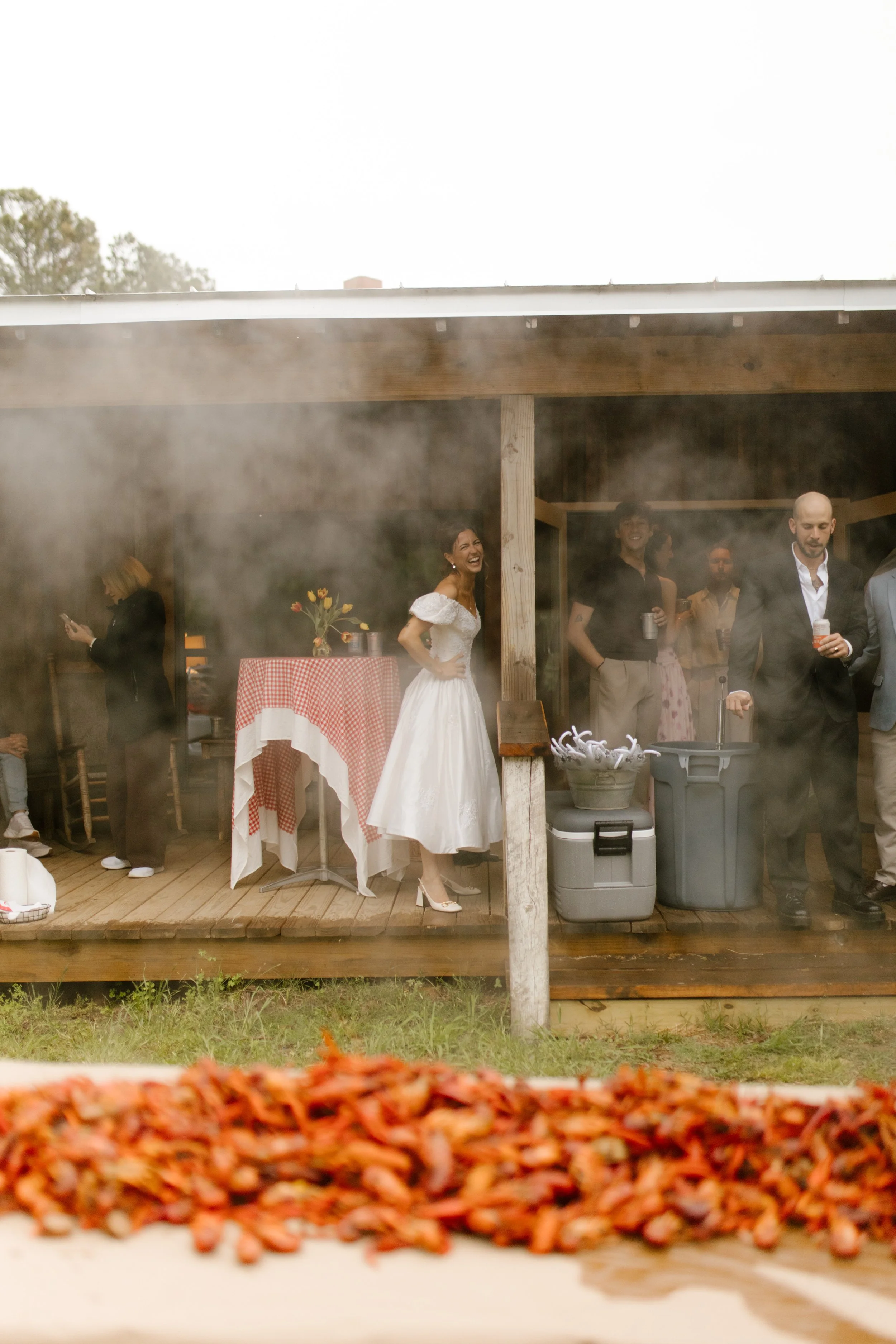 Outdoor crawfish boil setup with guests gathering on a covered porch during rehearsal dinner photography