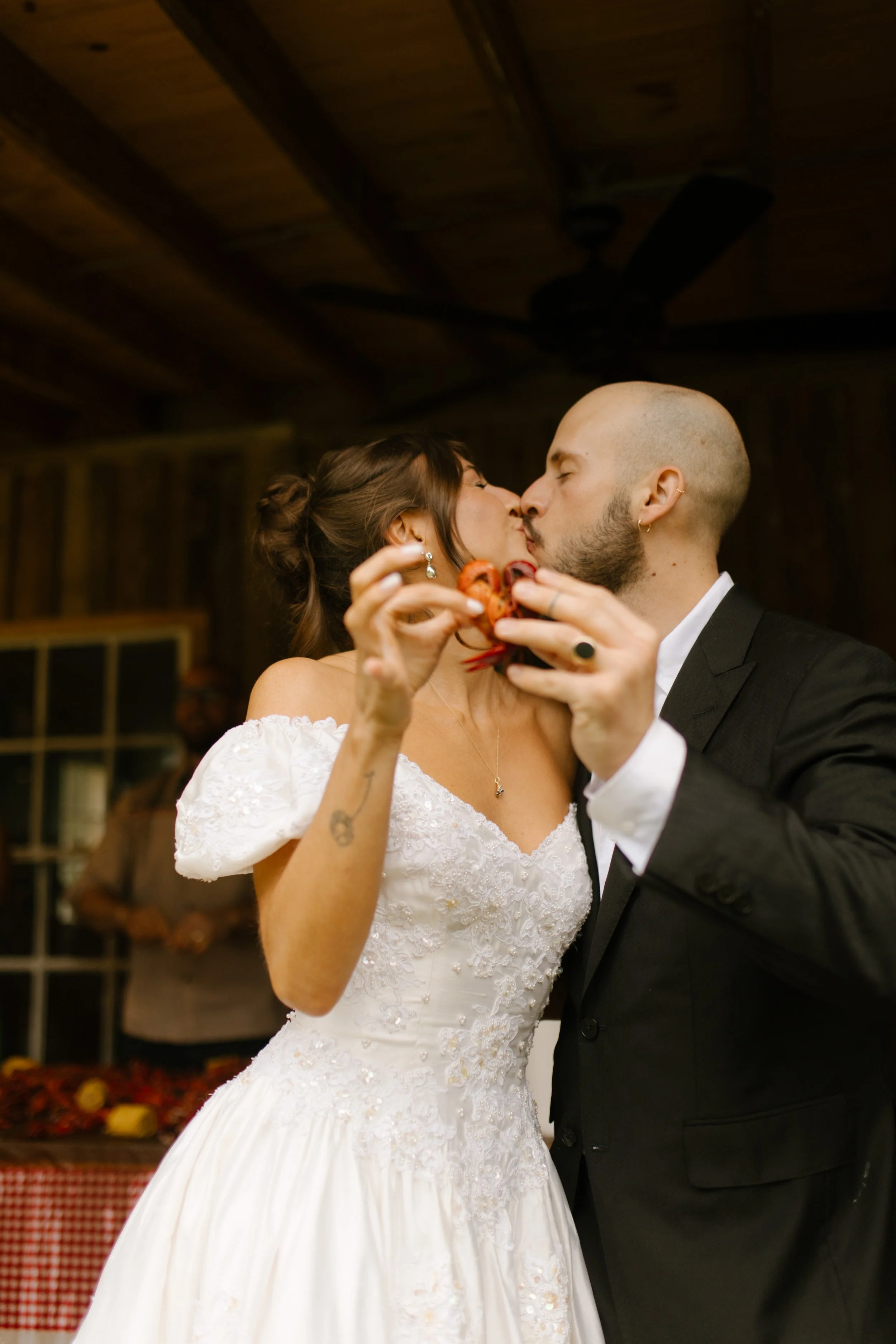 Bride and groom kiss while holding crawfish during rehearsal dinner photography at a Mississippi wedding weekend