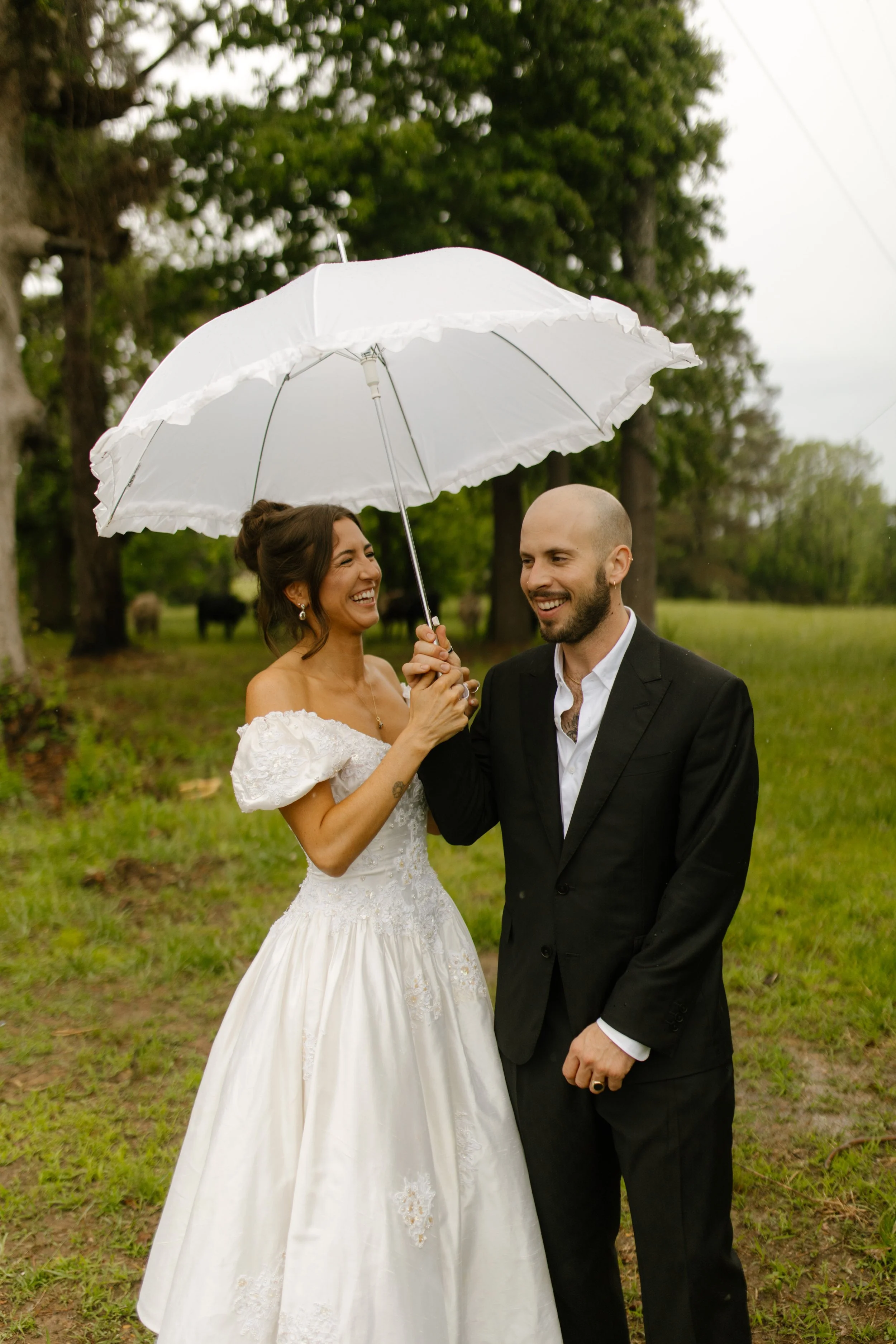 Couple laughing under a white umbrella during rainy rehearsal dinner photography portraits in Mississippi