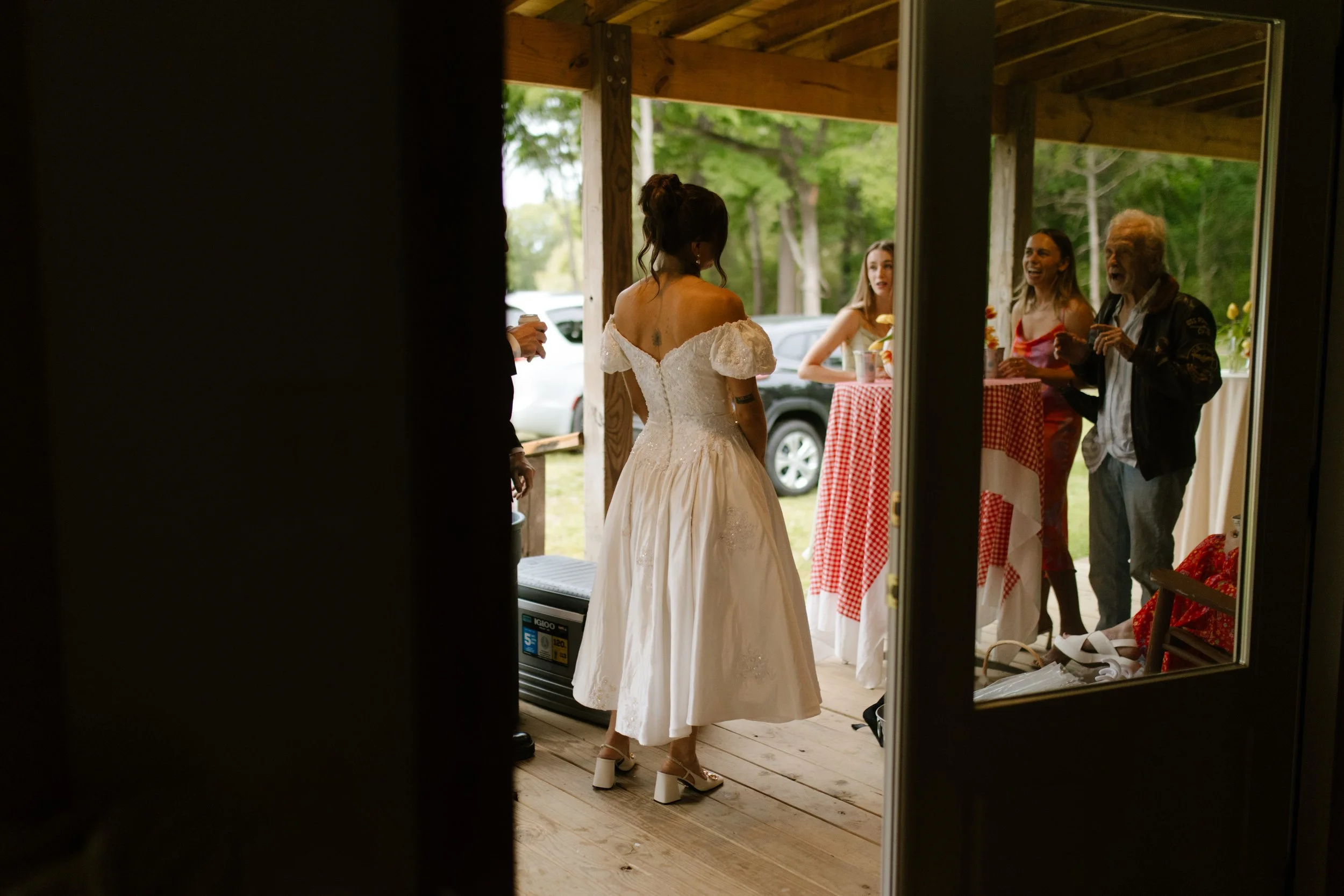 Bride greeting guests on the covered porch during a casual Southern wedding rehearsal dinner