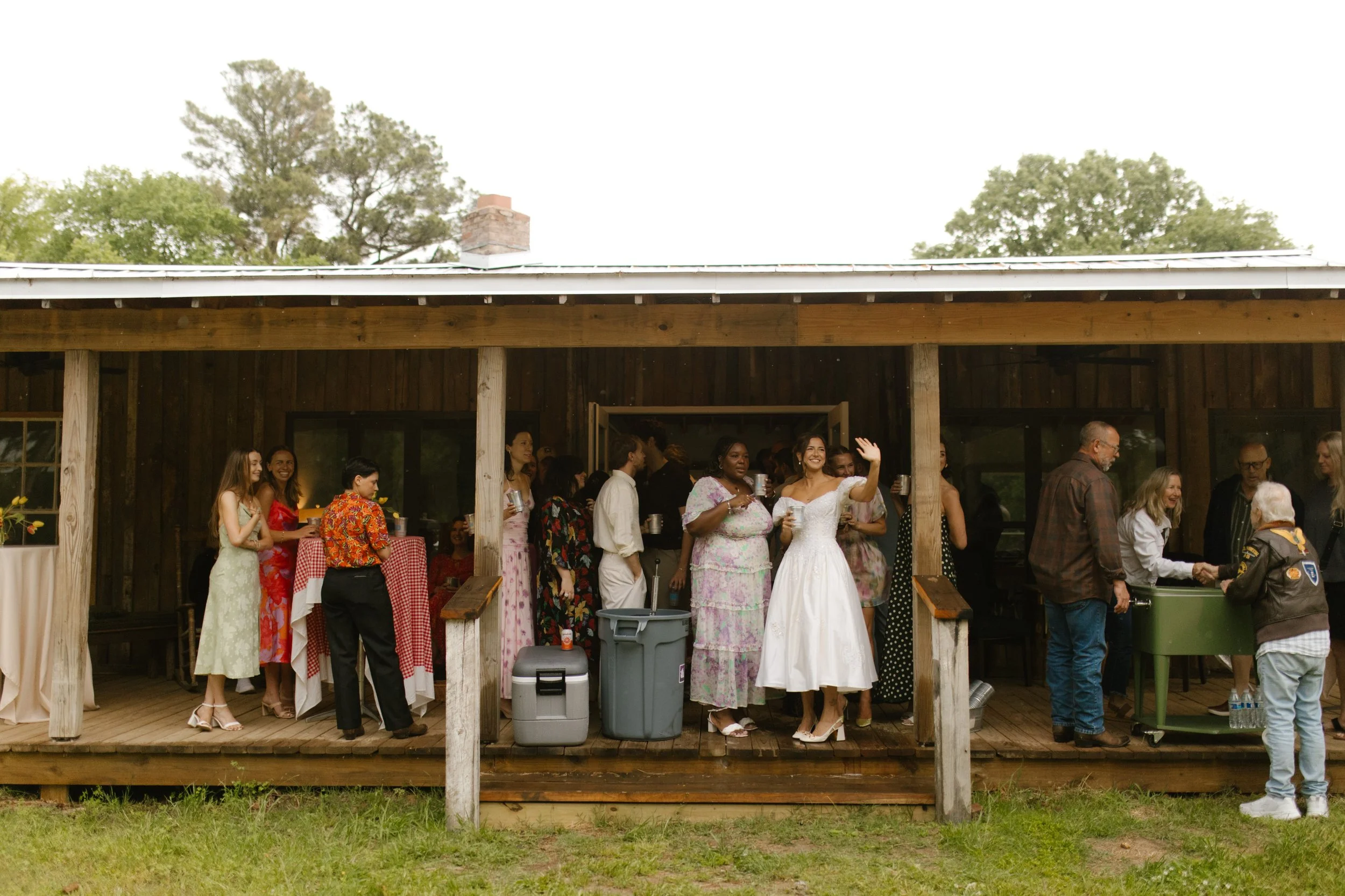 Guests gathering on a covered porch as the bride waves during rehearsal dinner photography at a Mississippi wedding