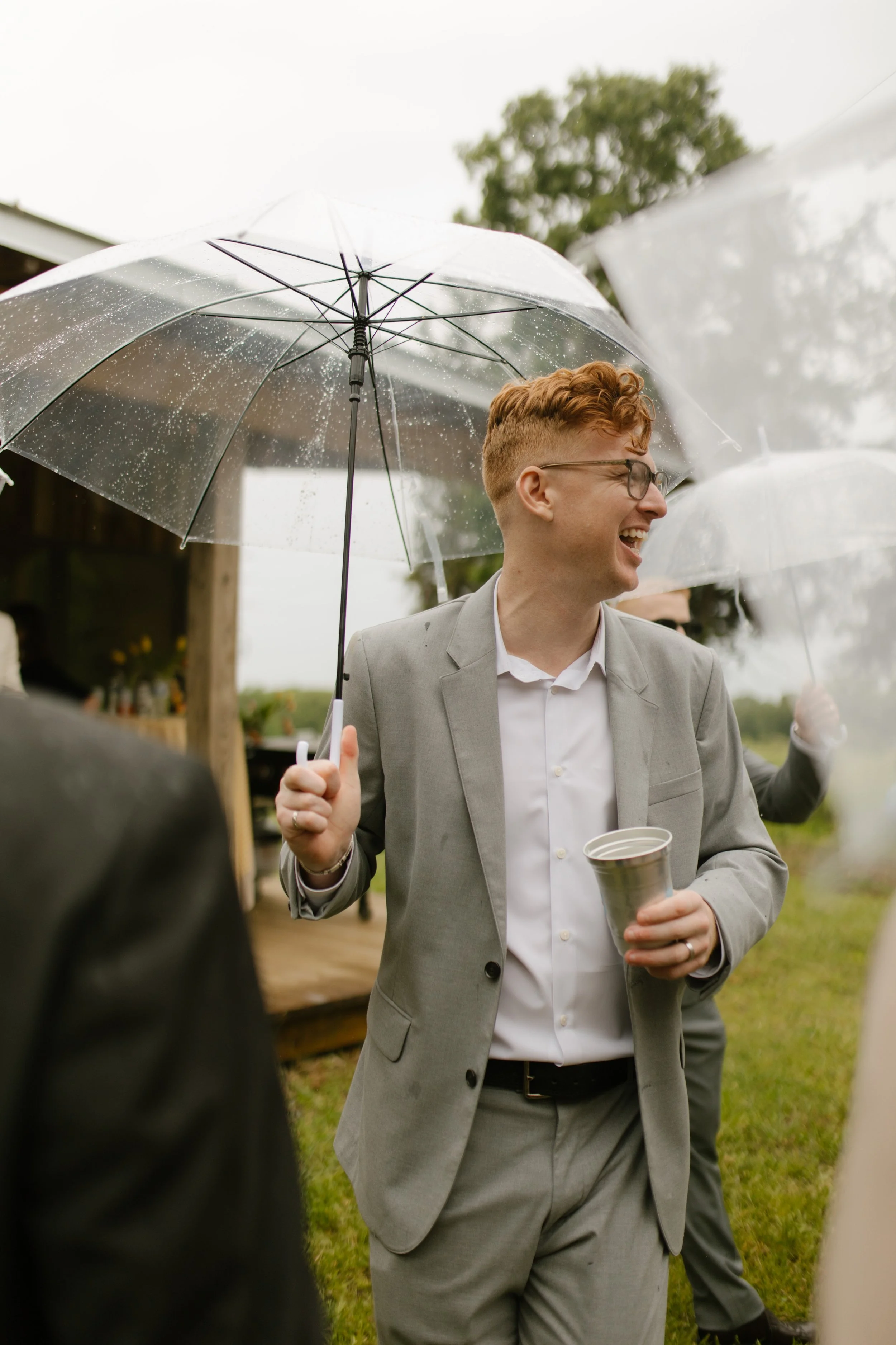 Wedding guest laughing under a clear umbrella during rainy rehearsal dinner photography in Mississippi