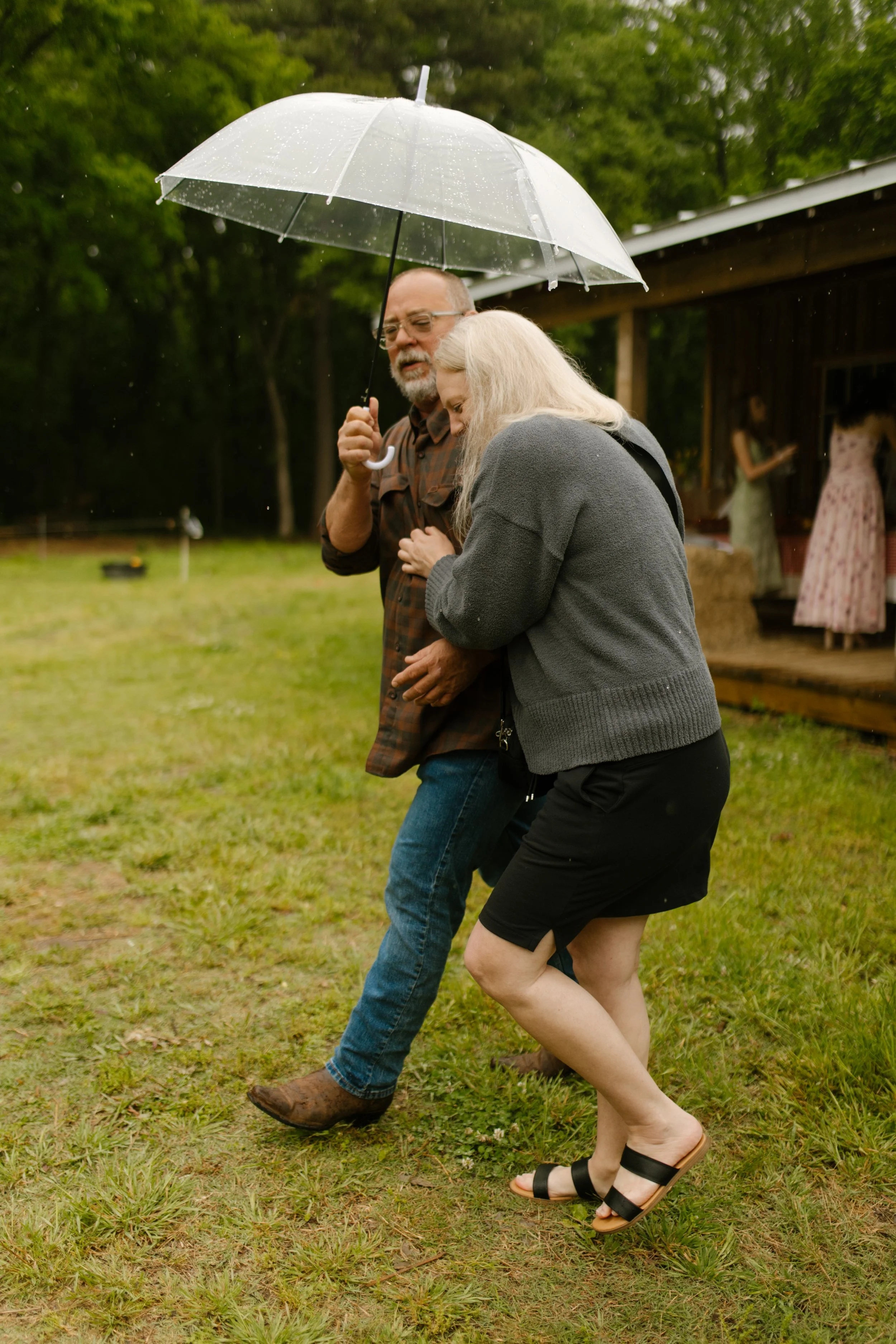 Family members walking across the lawn beneath an umbrella during a light rain shower before the celebration.