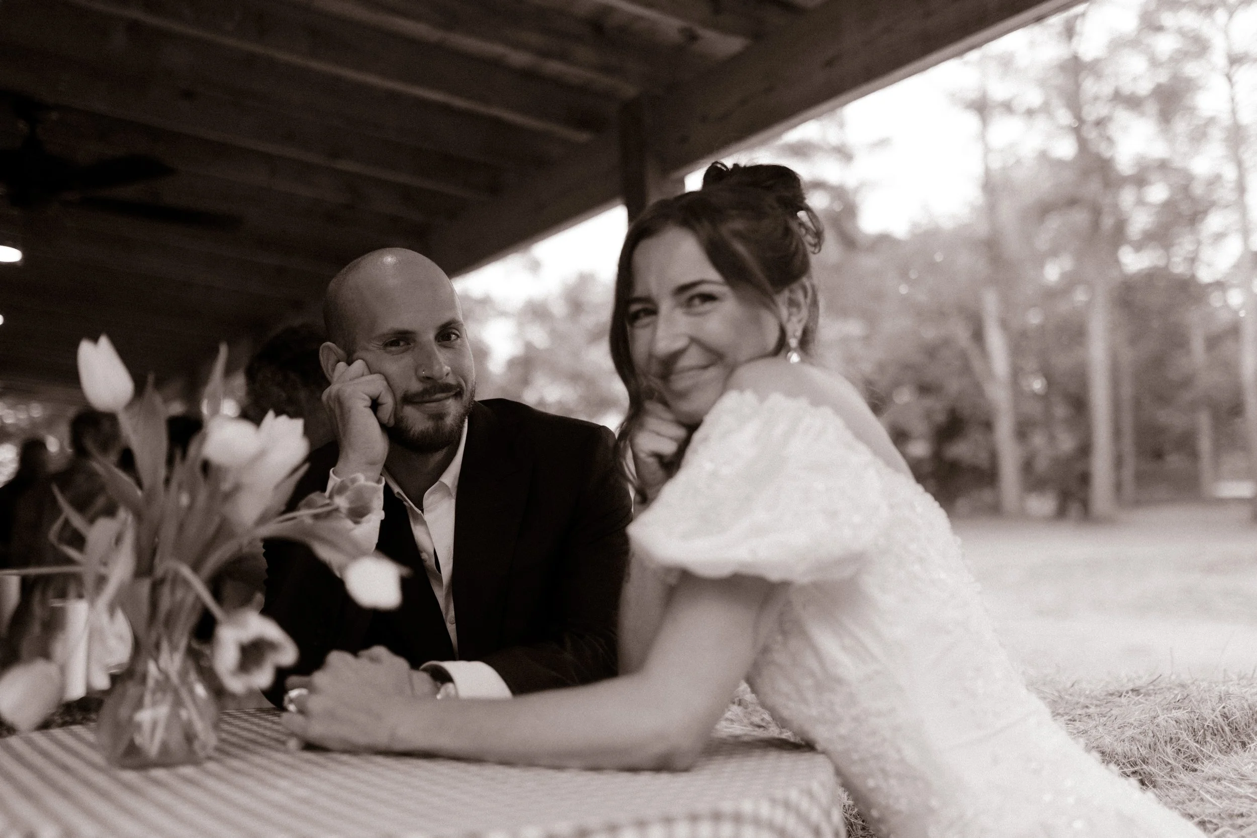 Bride and groom sitting together at a gingham-covered table during rehearsal dinner photography