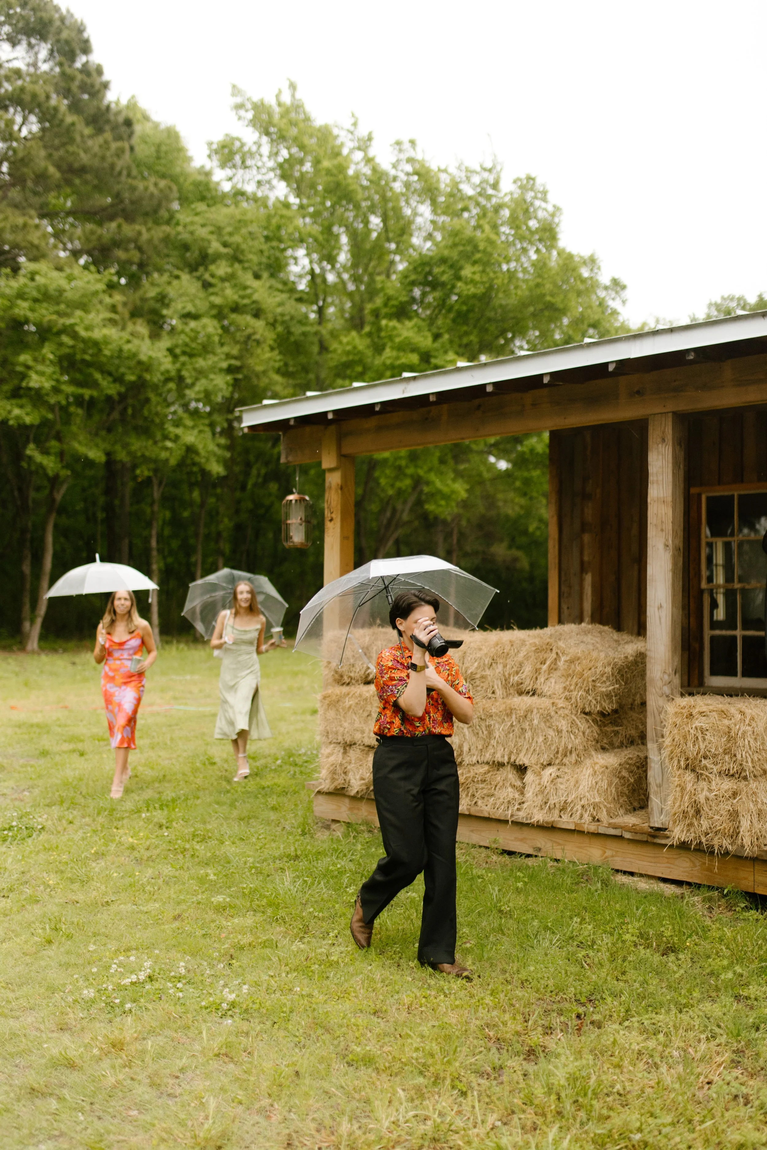 Guests carrying umbrellas across the lawn toward the covered venue during rehearsal dinner photography
