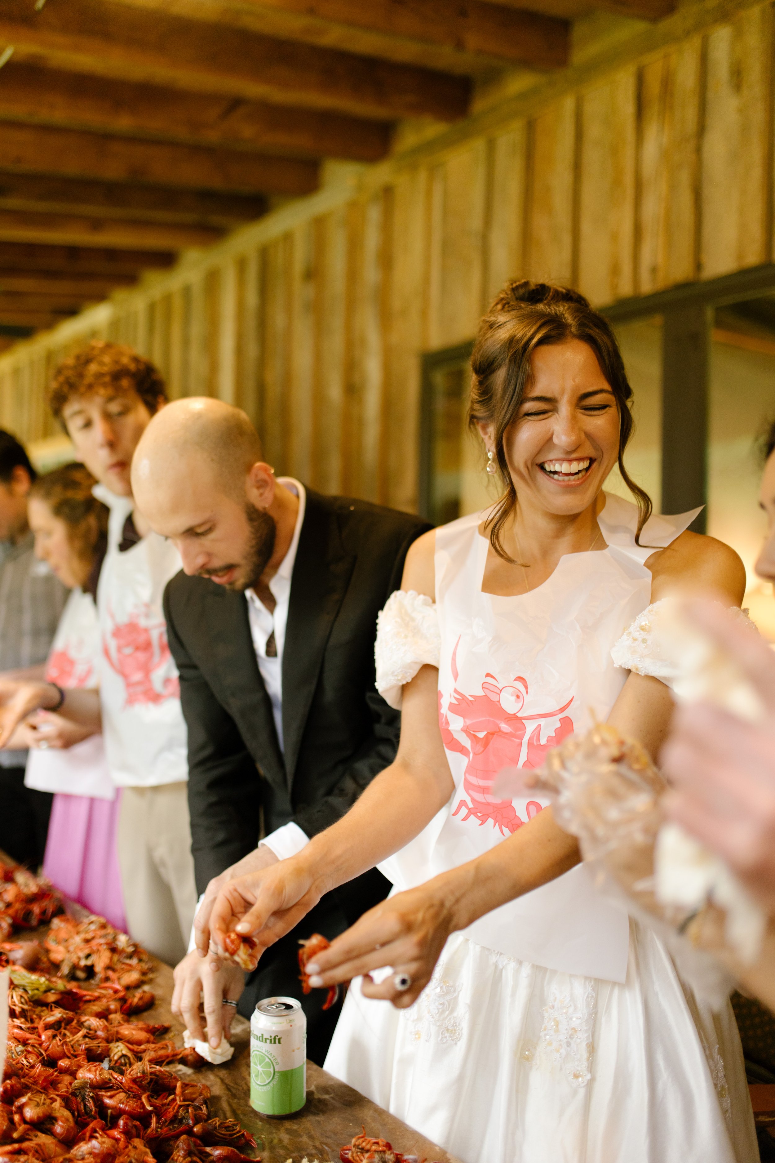 Bride and groom wearing crawfish bibs while laughing and enjoying a casual wedding rehearsal photography event with guests.