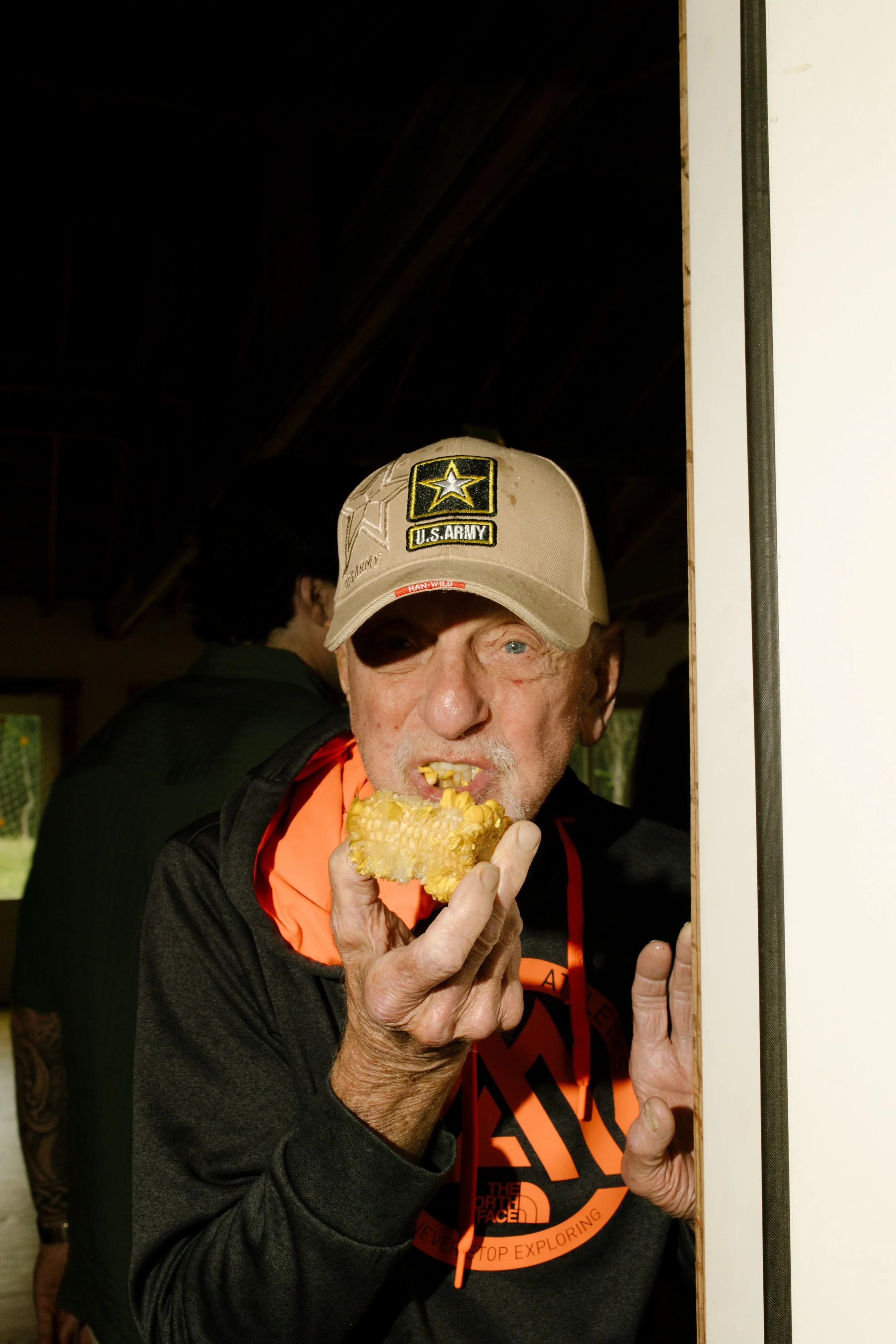 Wedding rehearsal dinner guest enjoying corn on the cob inside a rustic venue during a crawfish boil celebration.