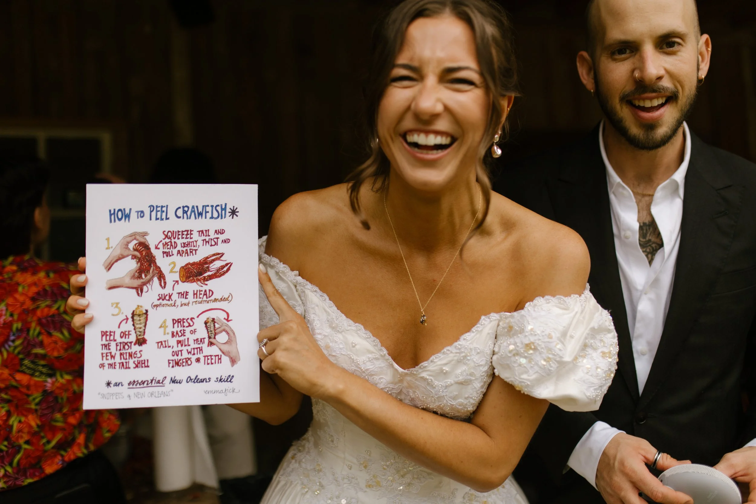 Bride holding a crawfish boil instruction sign and laughing during a fun wedding rehearsal dinner activity.