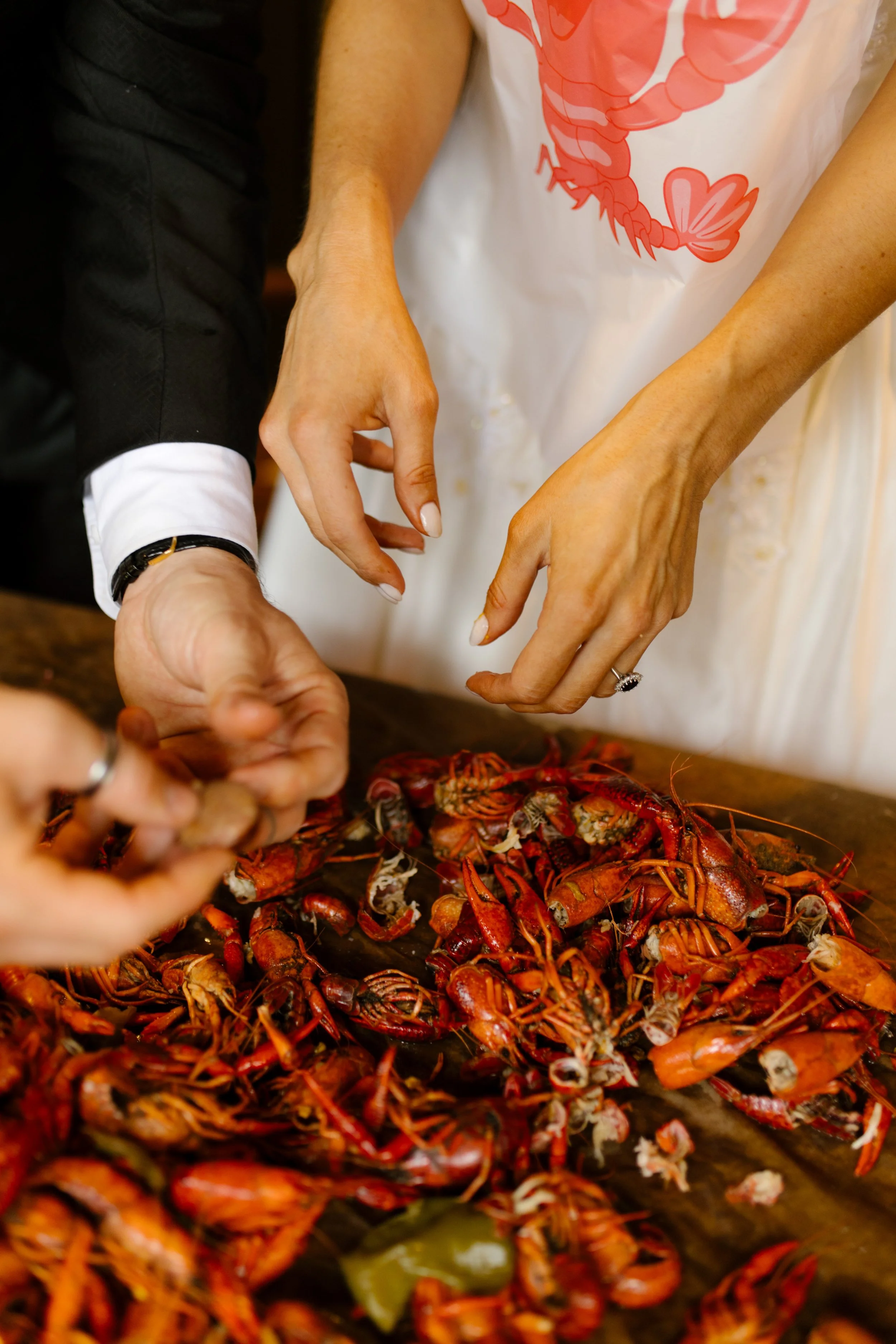 Groom and guests gathering around steaming crawfish tables during a lively wedding rehearsal photography celebration.