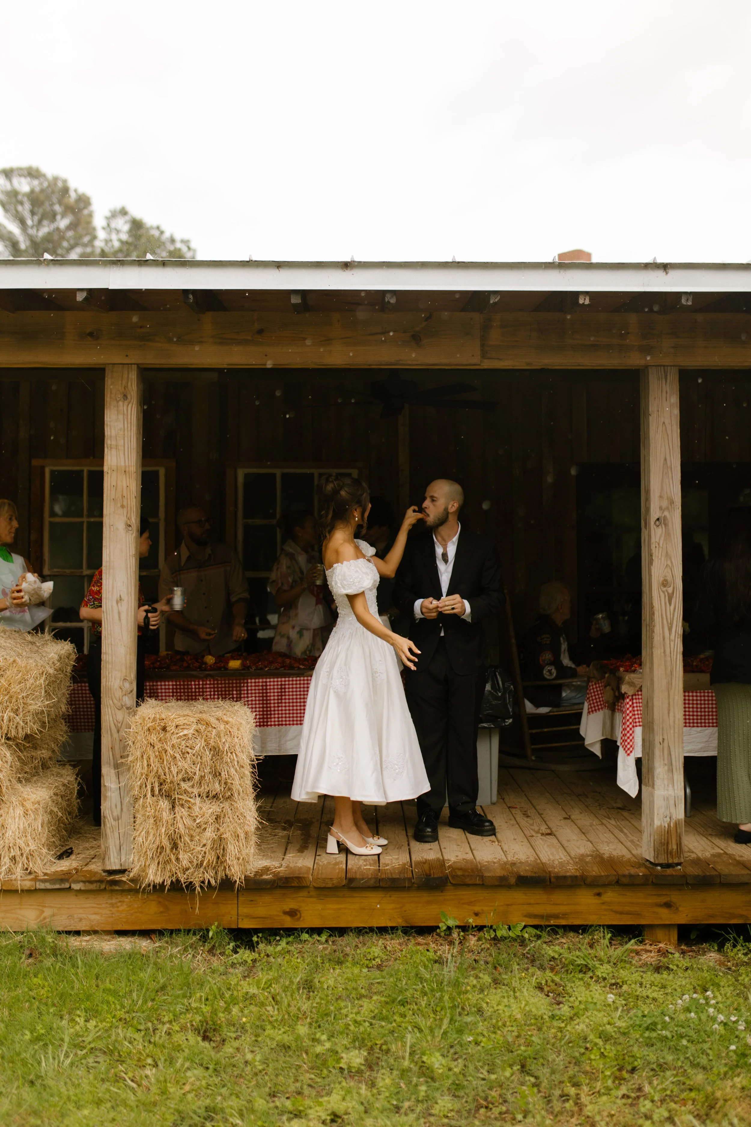 Bride playfully feeding the groom during a relaxed wedding rehearsal photography event on a rustic porch.