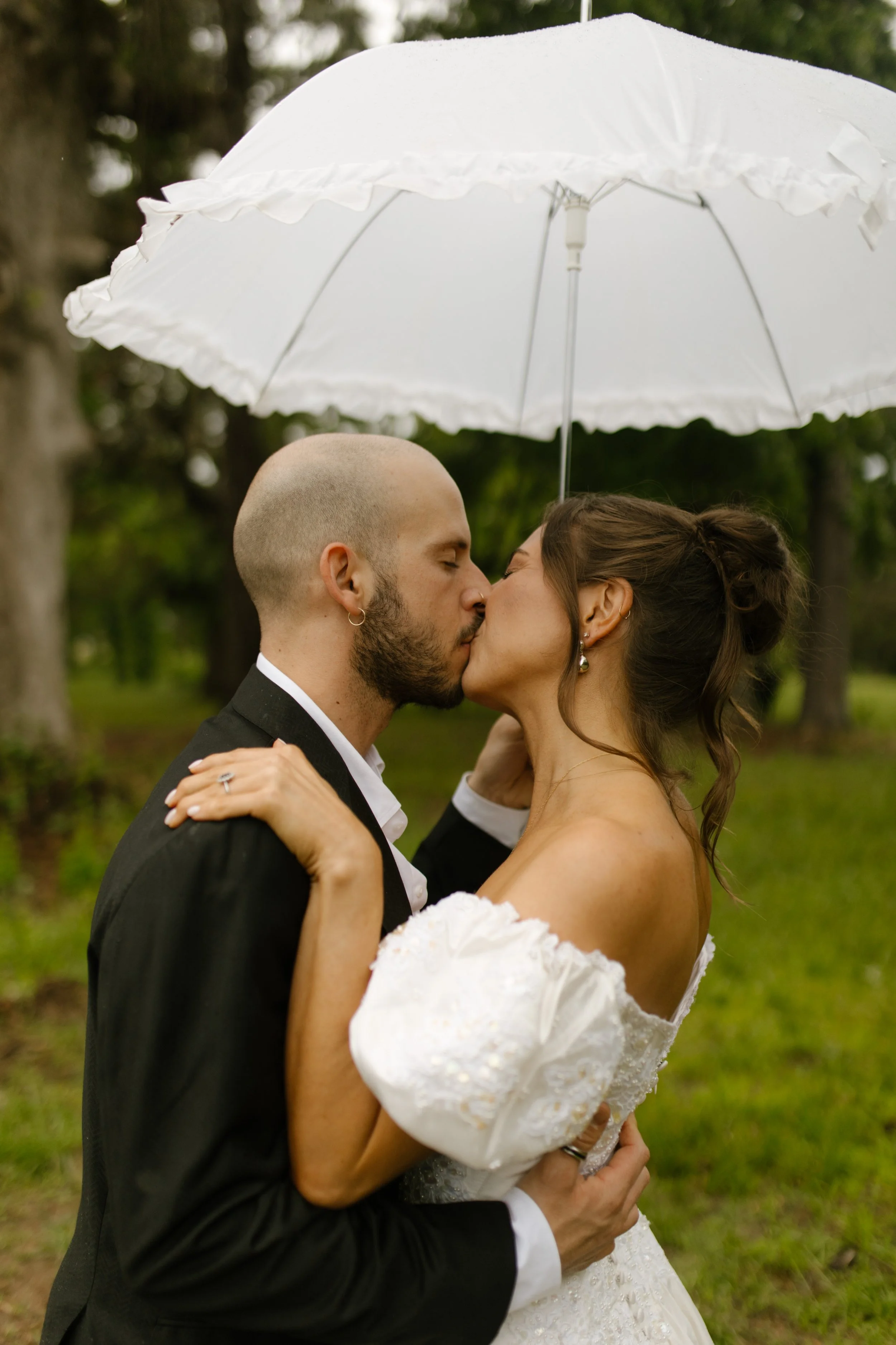 Bride and groom kissing beneath an umbrella during rehearsal dinner photography on a rainy wedding weekend