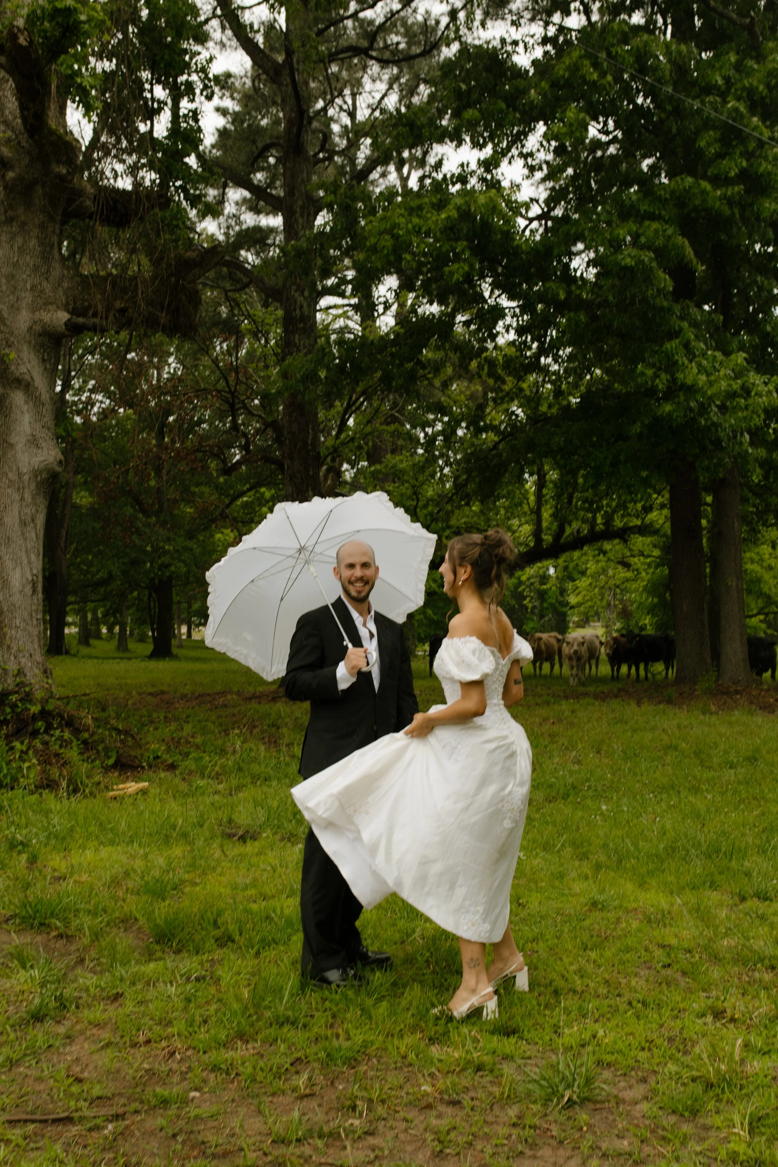 Couple posing in a grassy field with a white umbrella during rehearsal dinner photography portraits