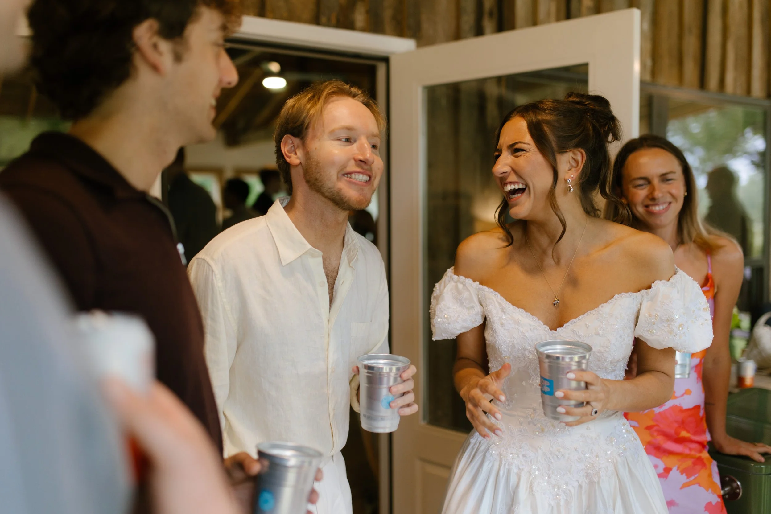 Bride laughing with friends while holding drinks at a wedding rehearsal dinner