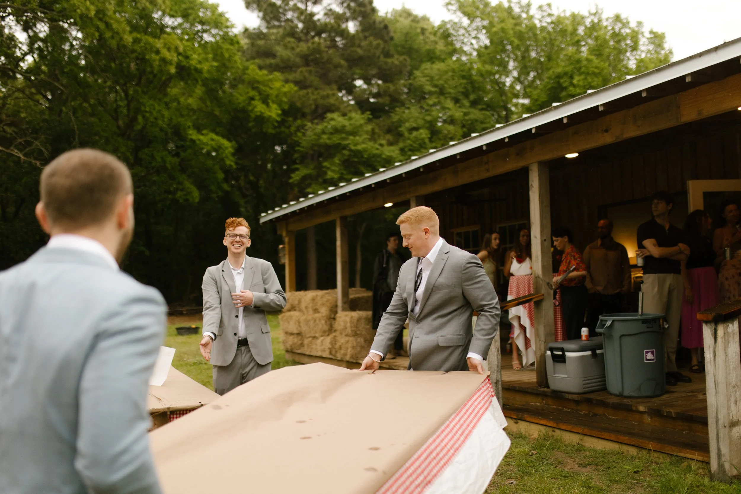 Wedding rehearsal photography captures guests setting up tables outside a rustic venue before the crawfish boil begins.