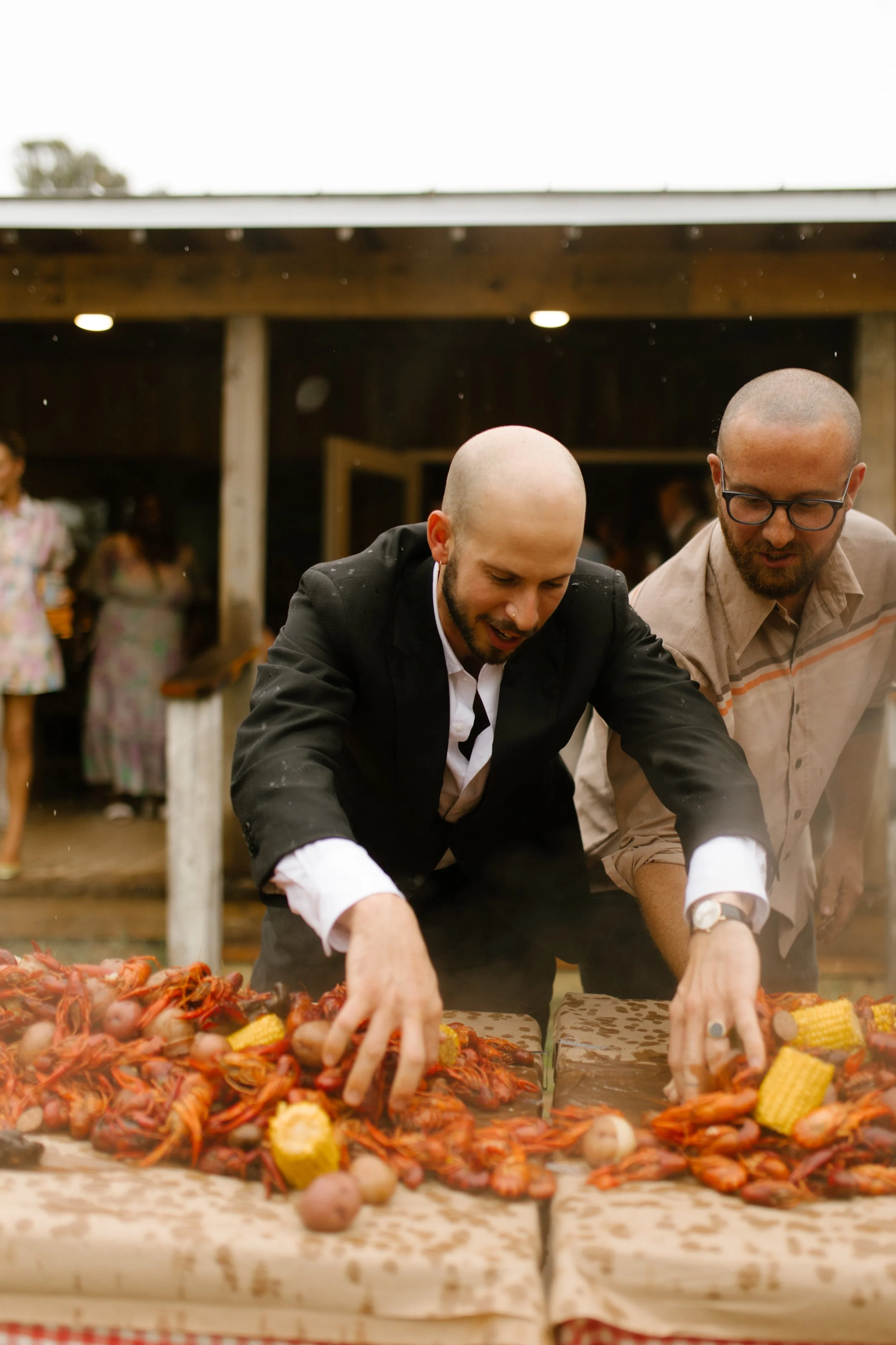 Groom and guest reaching for crawfish, corn, and potatoes during a lively wedding rehearsal photography celebration.
