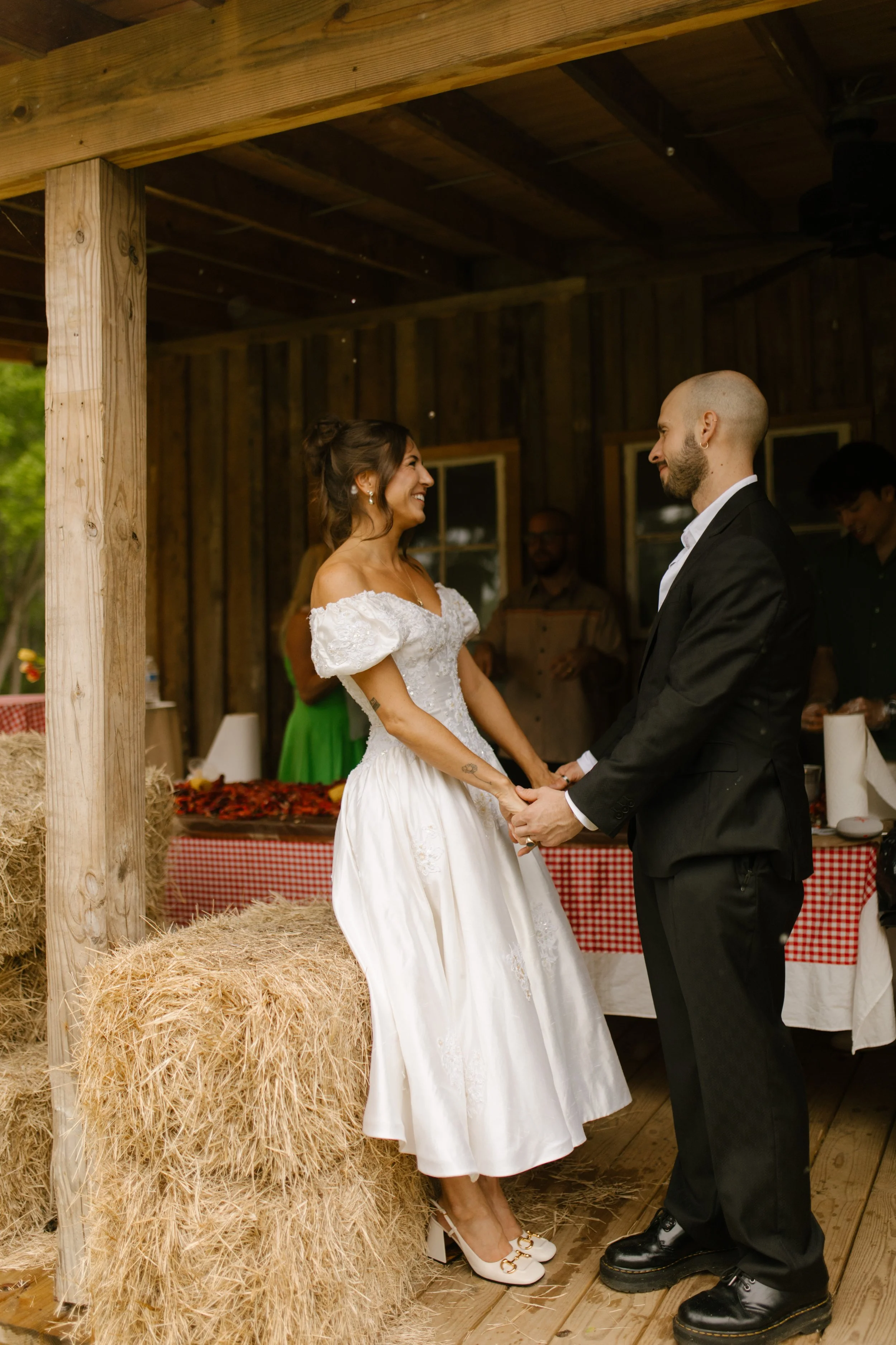 Bride and groom holding hands beside hay bales during an intimate wedding rehearsal photography moment on a covered porch.