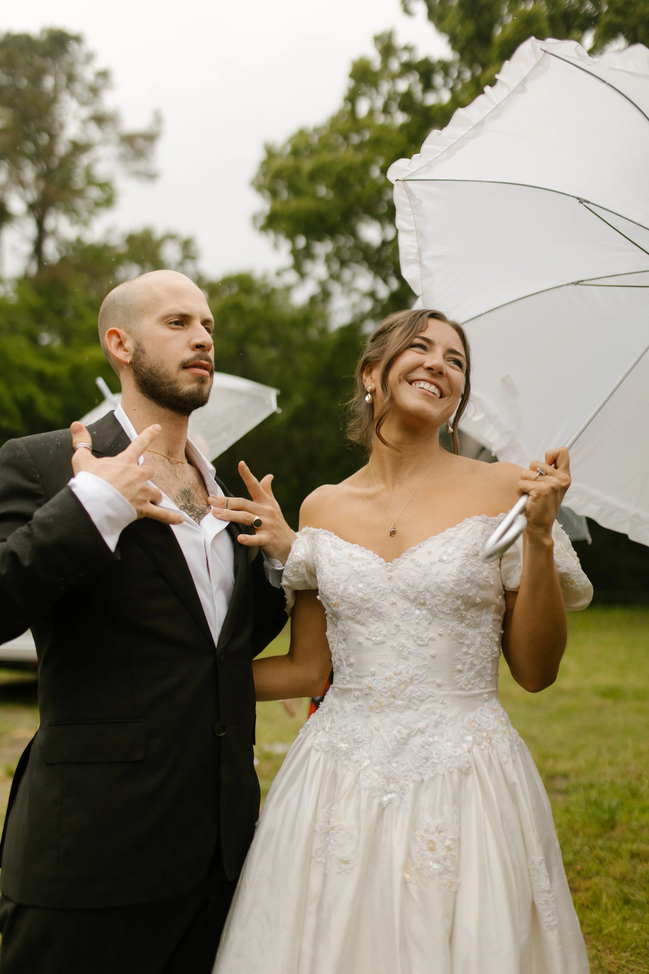 Bride smiling beneath a white umbrella while standing with the groom during a rainy wedding rehearsal photography event.