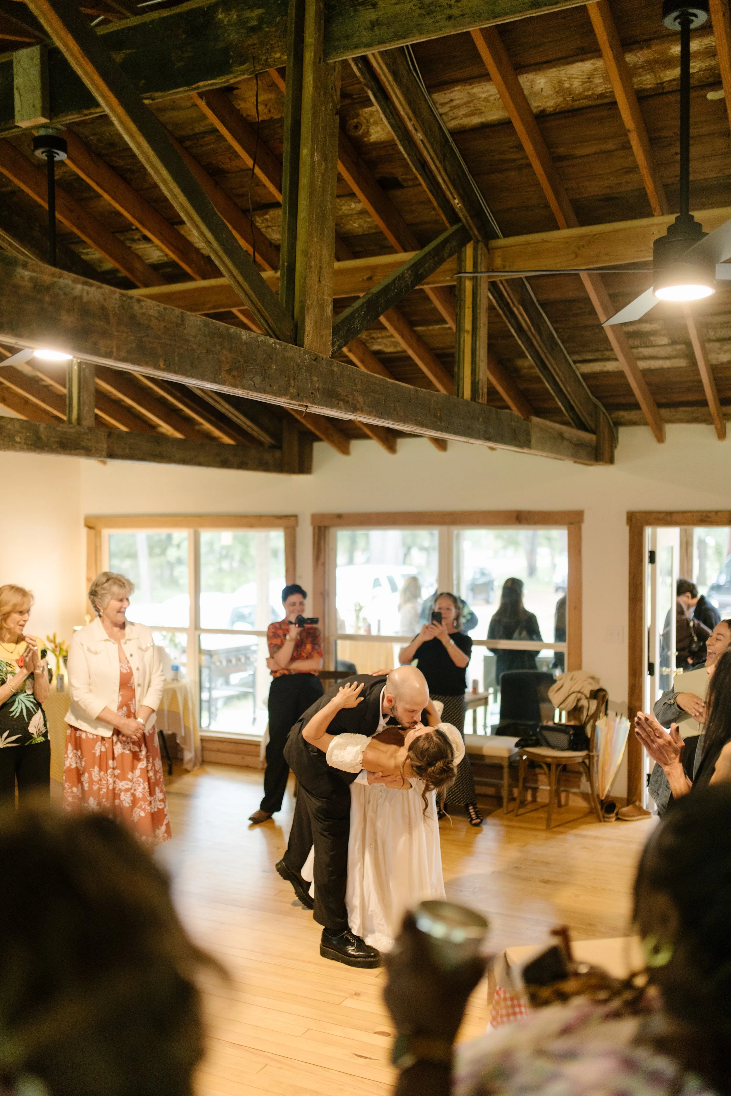 Bride and groom sharing a dance inside a rustic reception hall surrounded by family and friends.