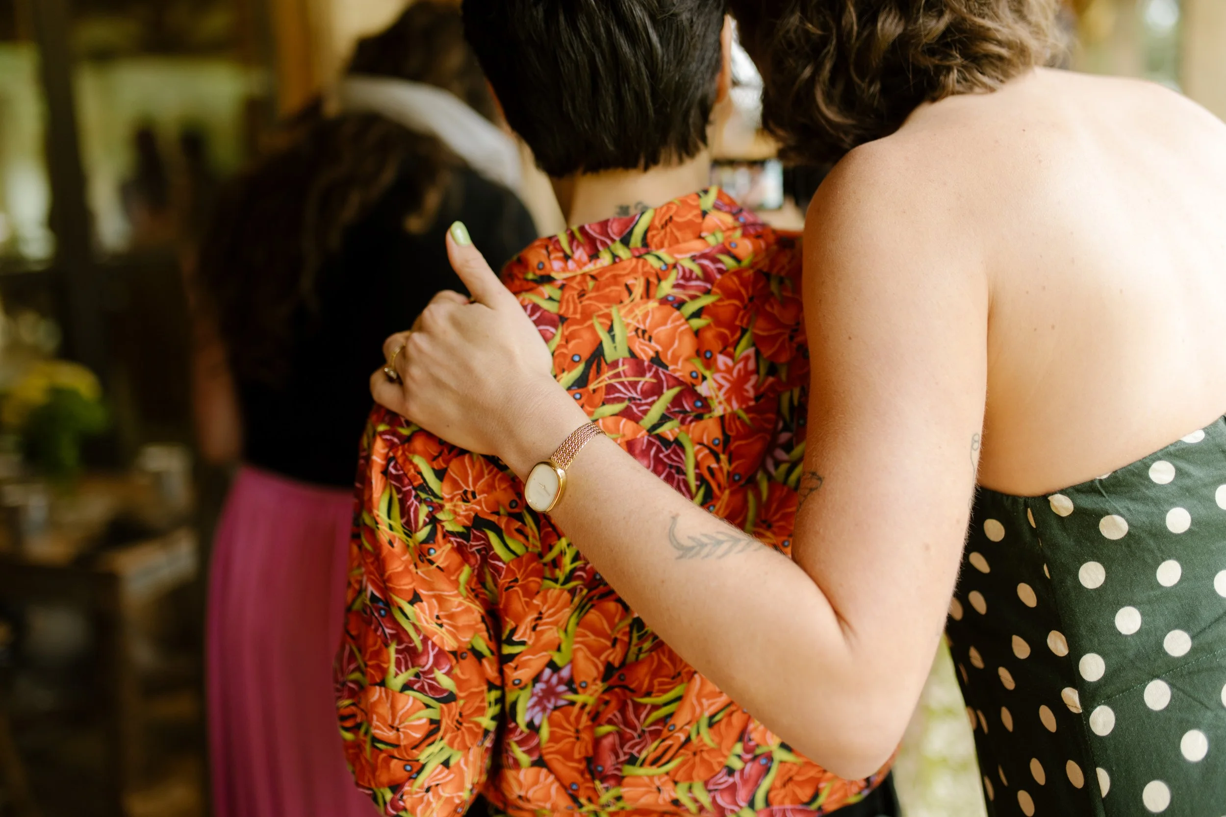 Guest placing an arm around a friend while chatting during a relaxed wedding rehearsal photography gathering.