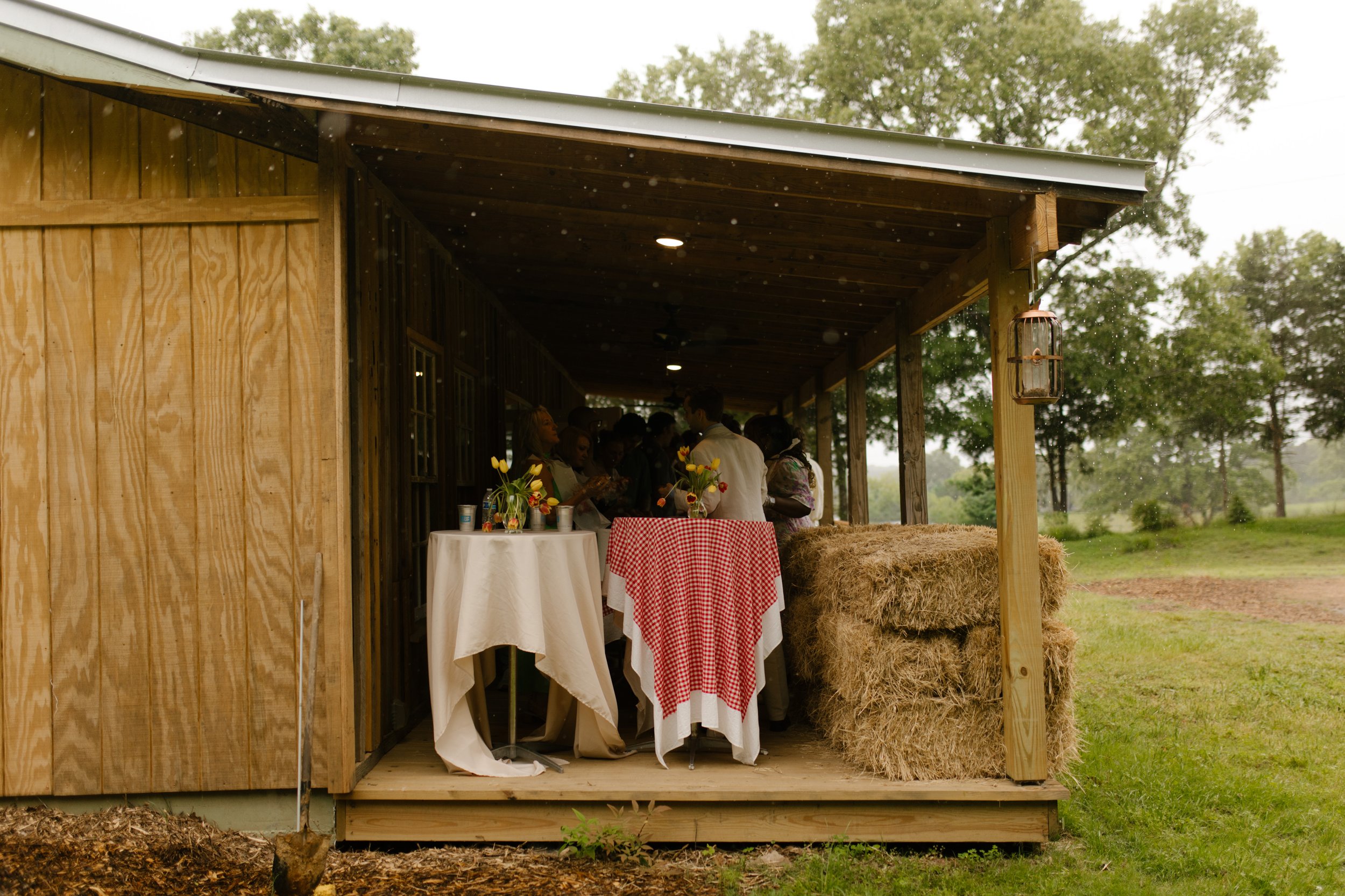 Rustic covered porch decorated with gingham linens and hay bales for a wedding rehearsal dinner