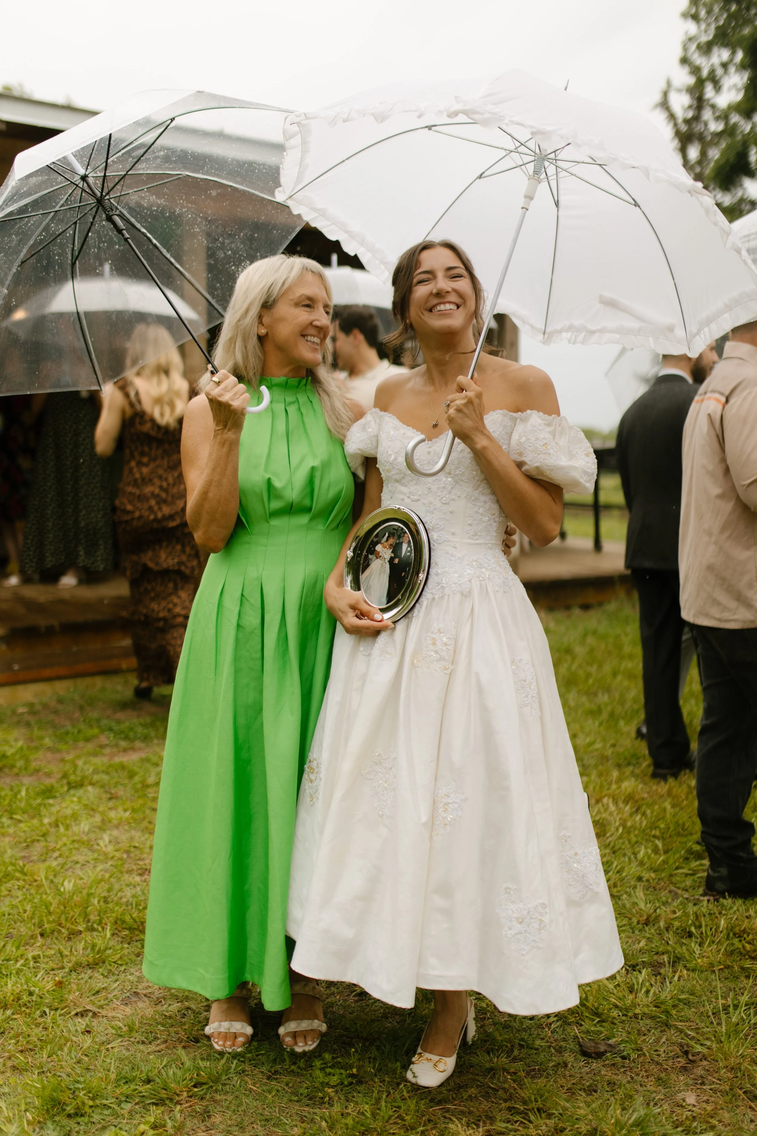 Bride posing with her mother while holding a framed family wedding photo during rehearsal dinner photography
