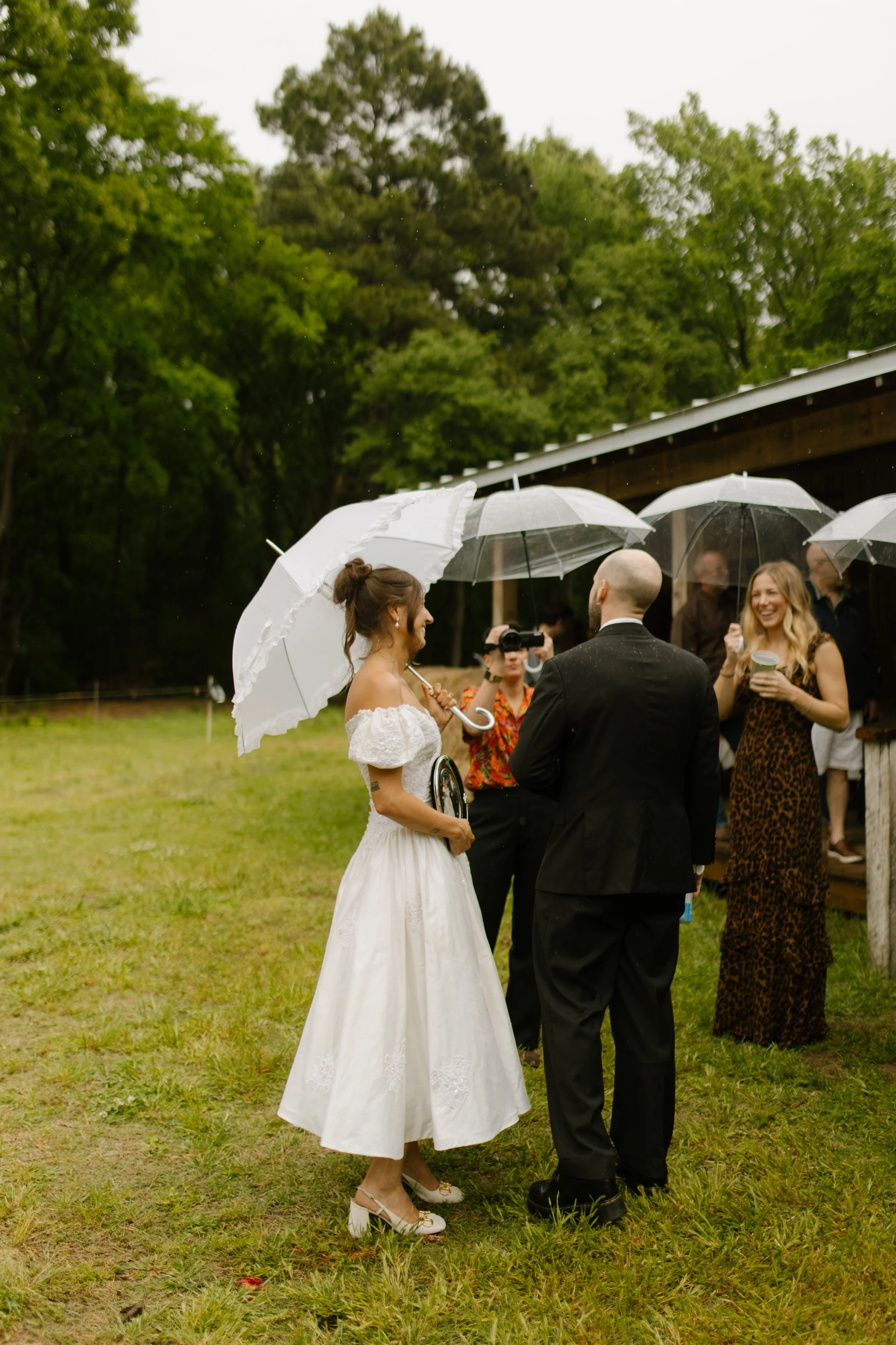 Bride and groom talking with guests under umbrellas during rainy rehearsal dinner photography