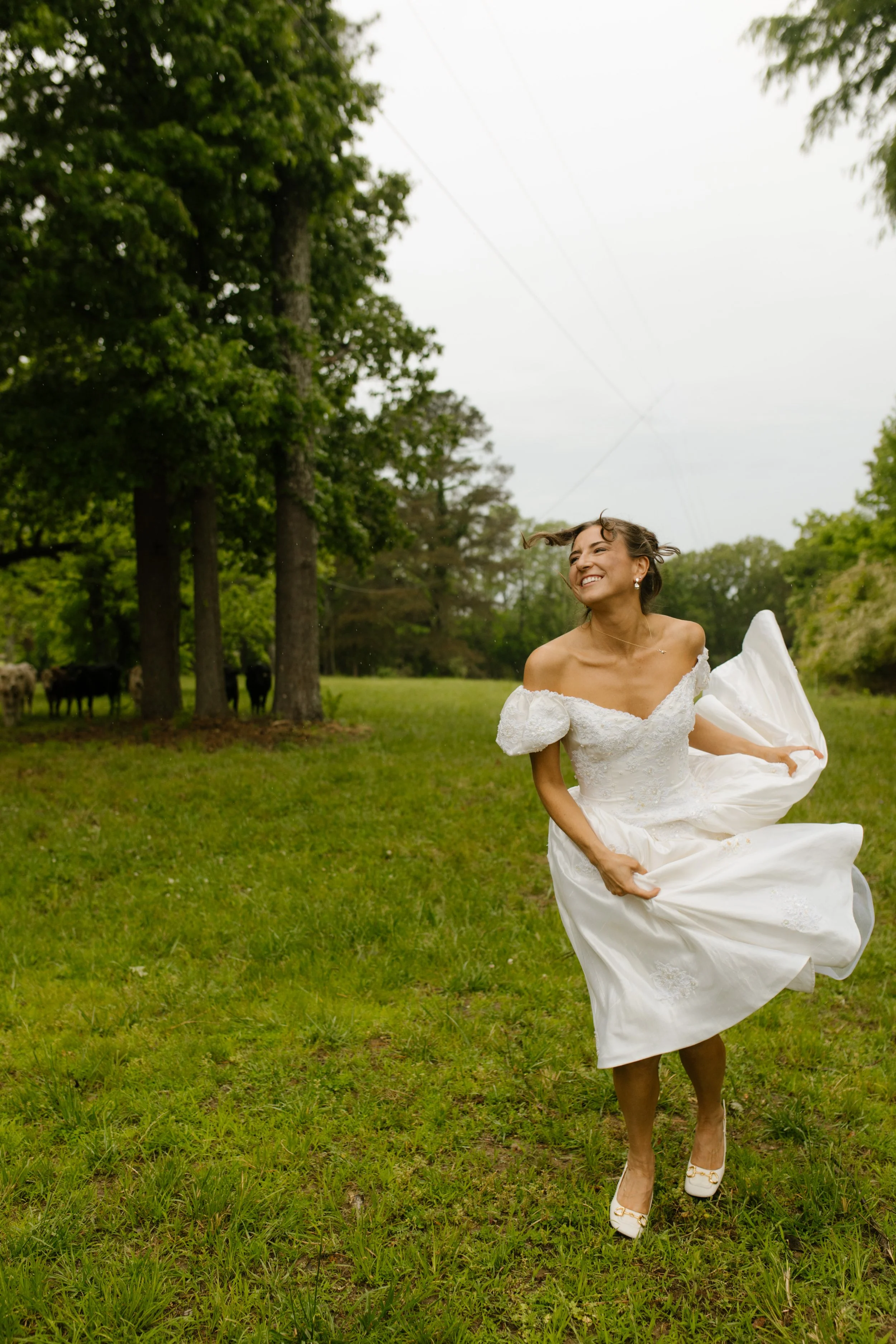 Bride twirling in her wedding dress across a grassy field as rain falls softly around her.