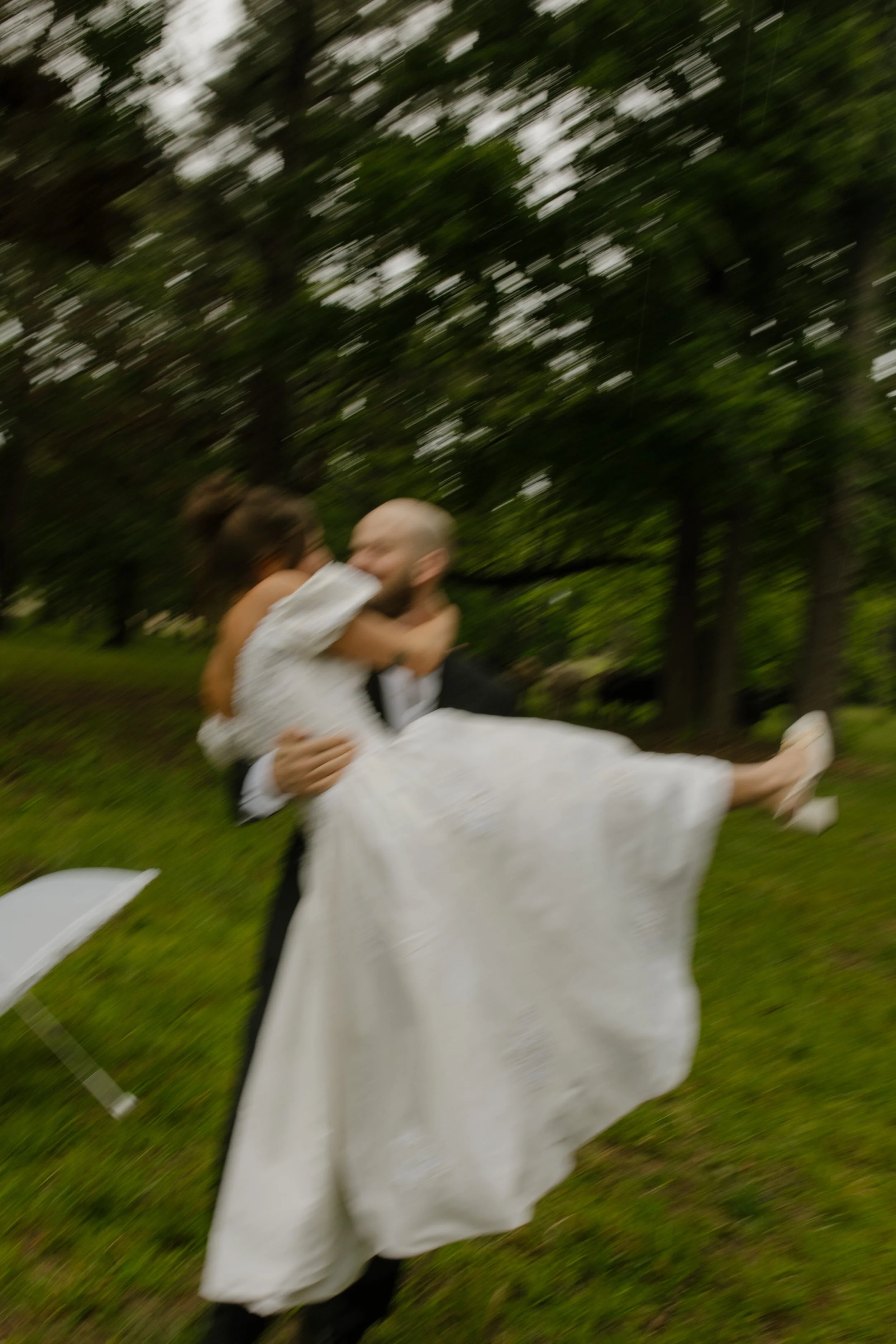 Groom lifting the bride in a playful embrace during wedding rehearsal photography in the rain.