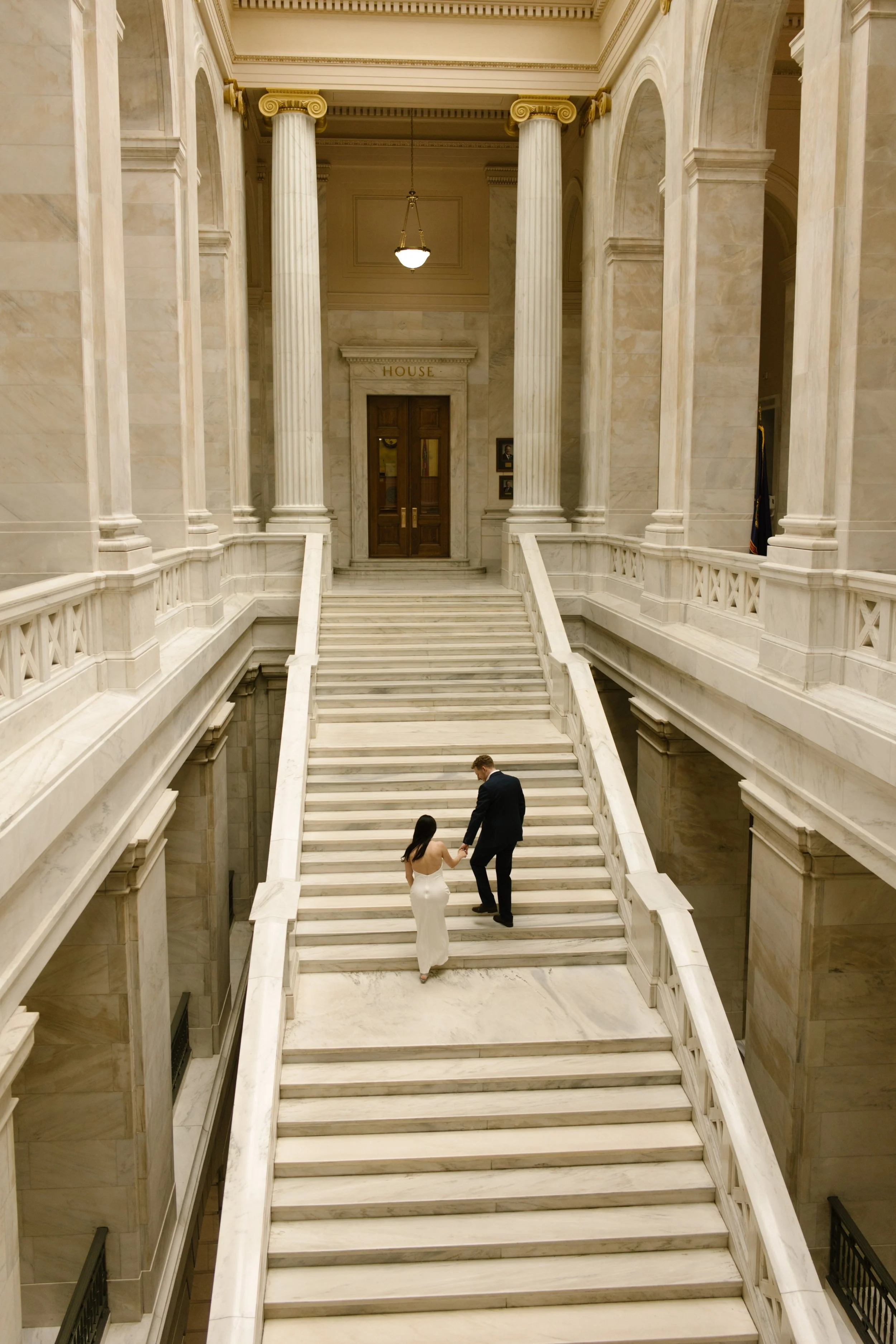 Couple walking hand in hand up the marble staircase at the Little Rock Courthouse