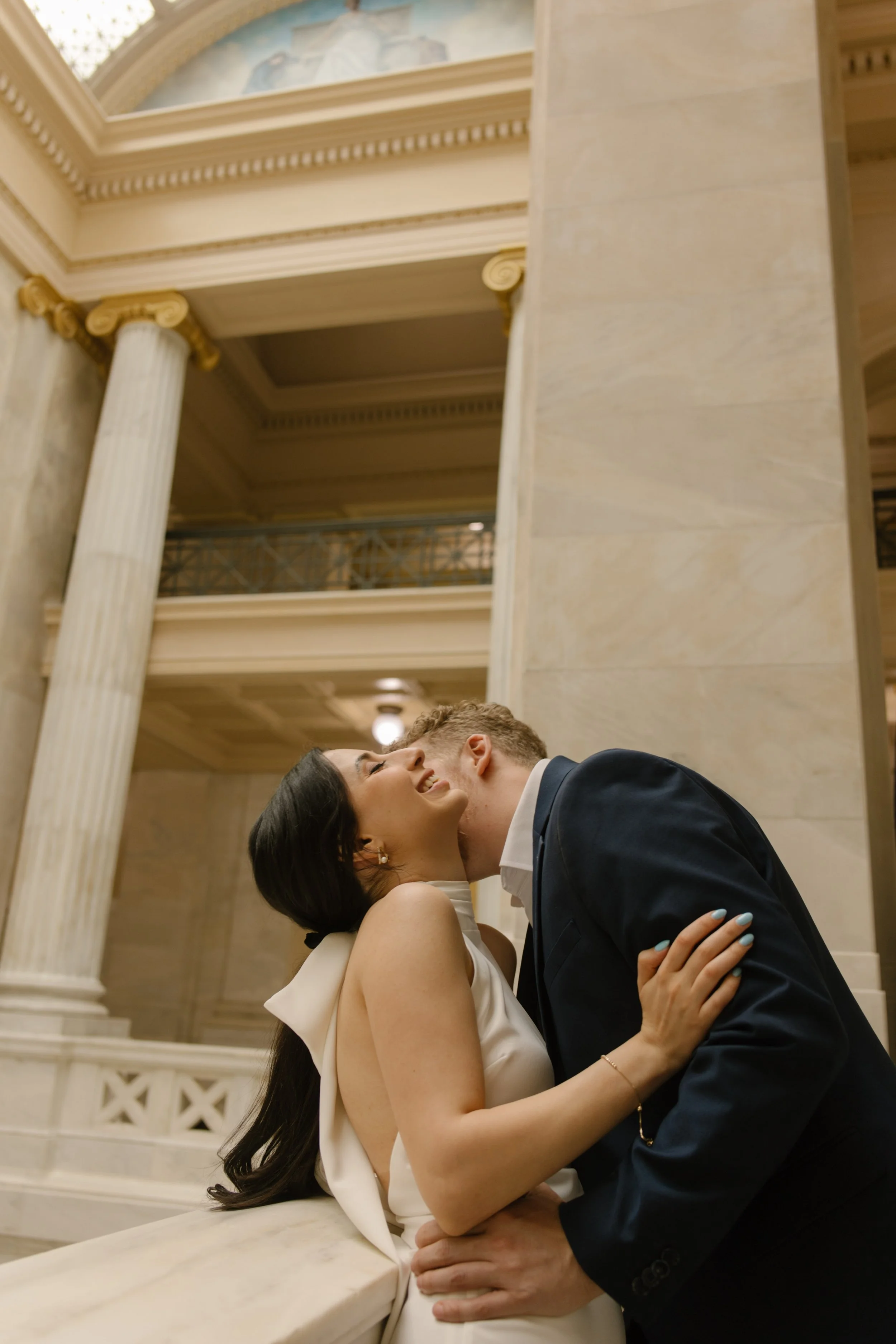 Couple embracing along a marble railing during a stylish courthouse engagement session