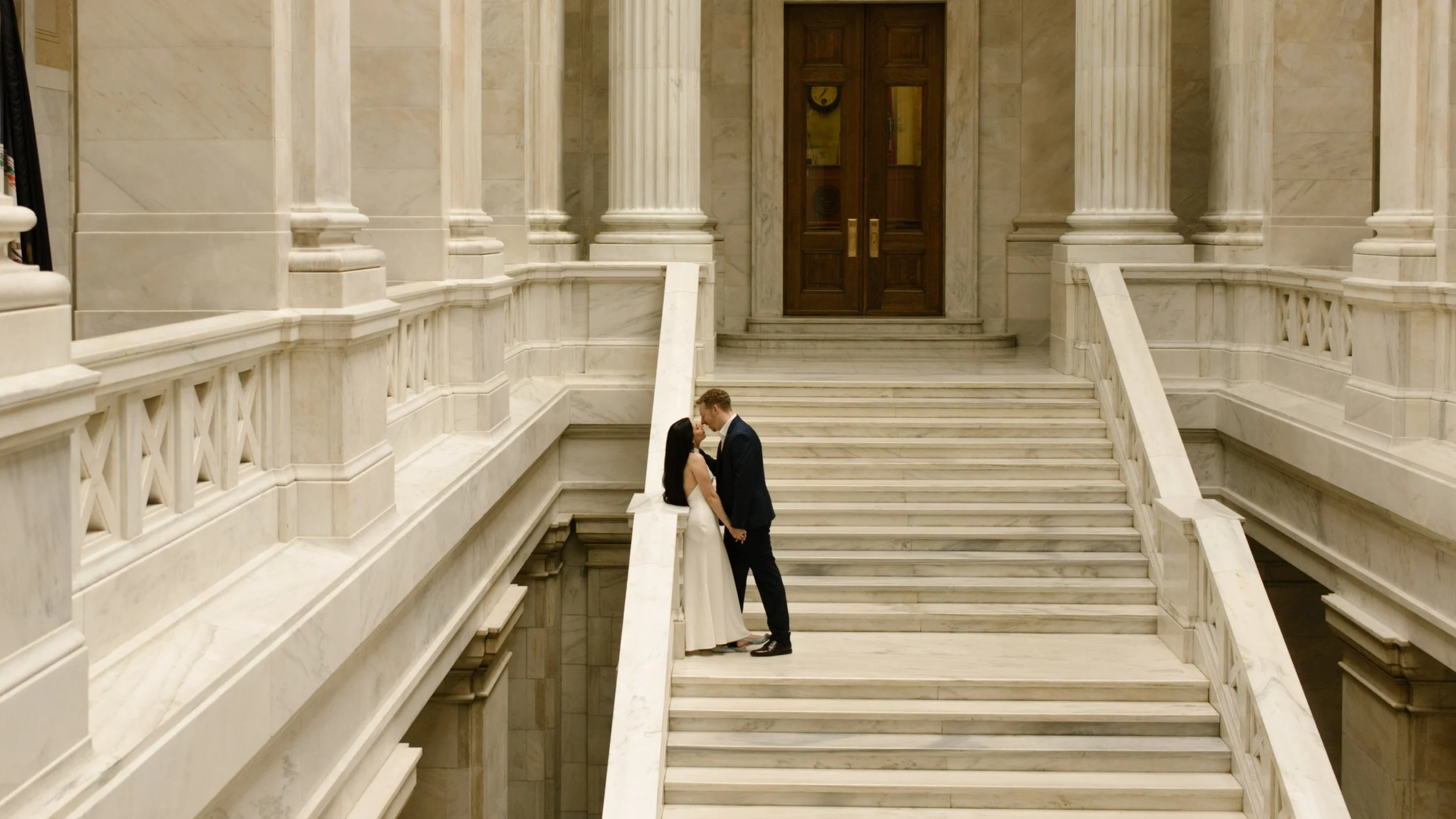 Couple embracing along a marble railing during a stylish courthouse engagement session