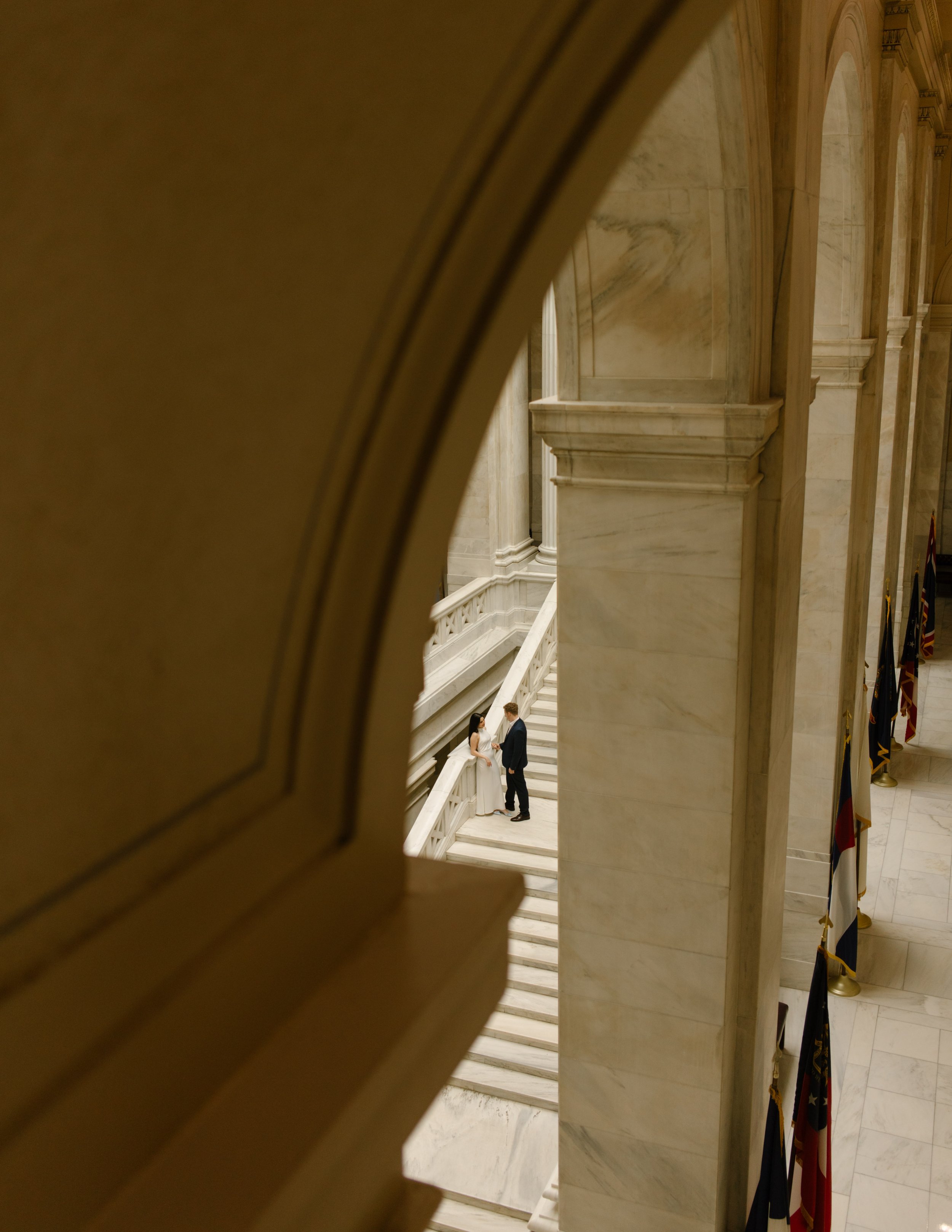 Wide architectural view of the Little Rock courthouse with a couple standing together on an upper staircase.