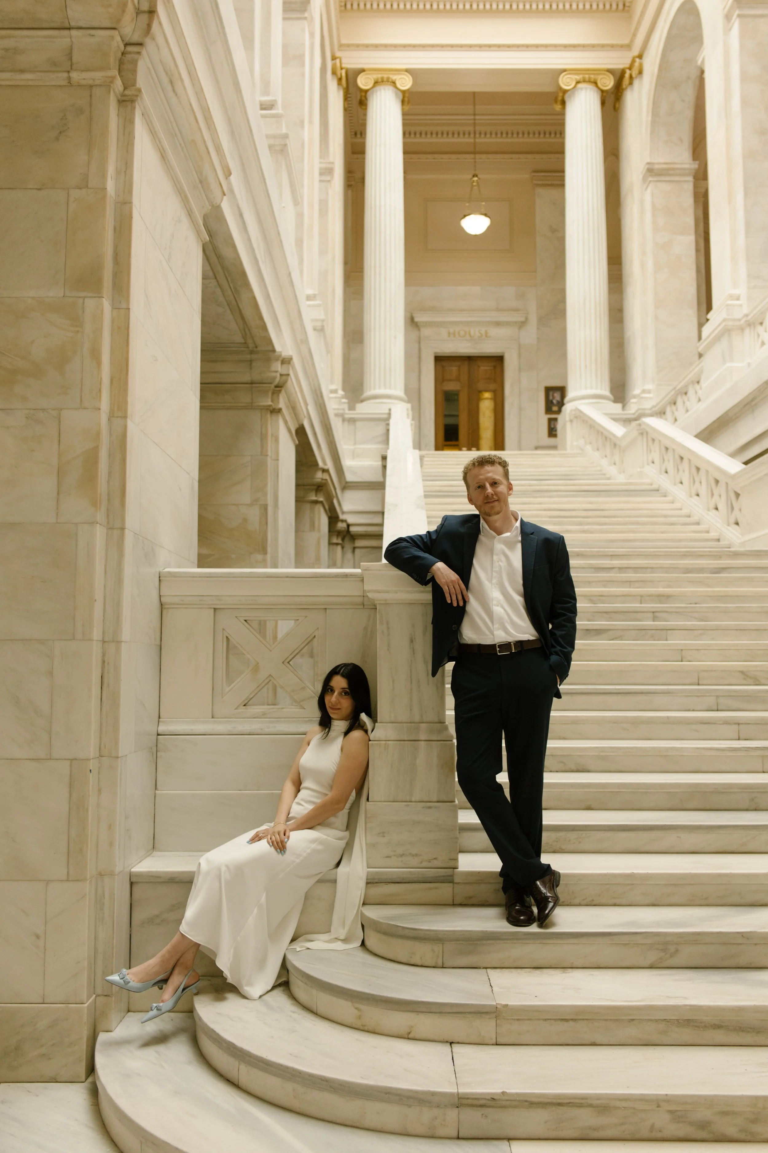 Stylish couple posing on curved marble stairs inside the historic Little Rock courthouse.