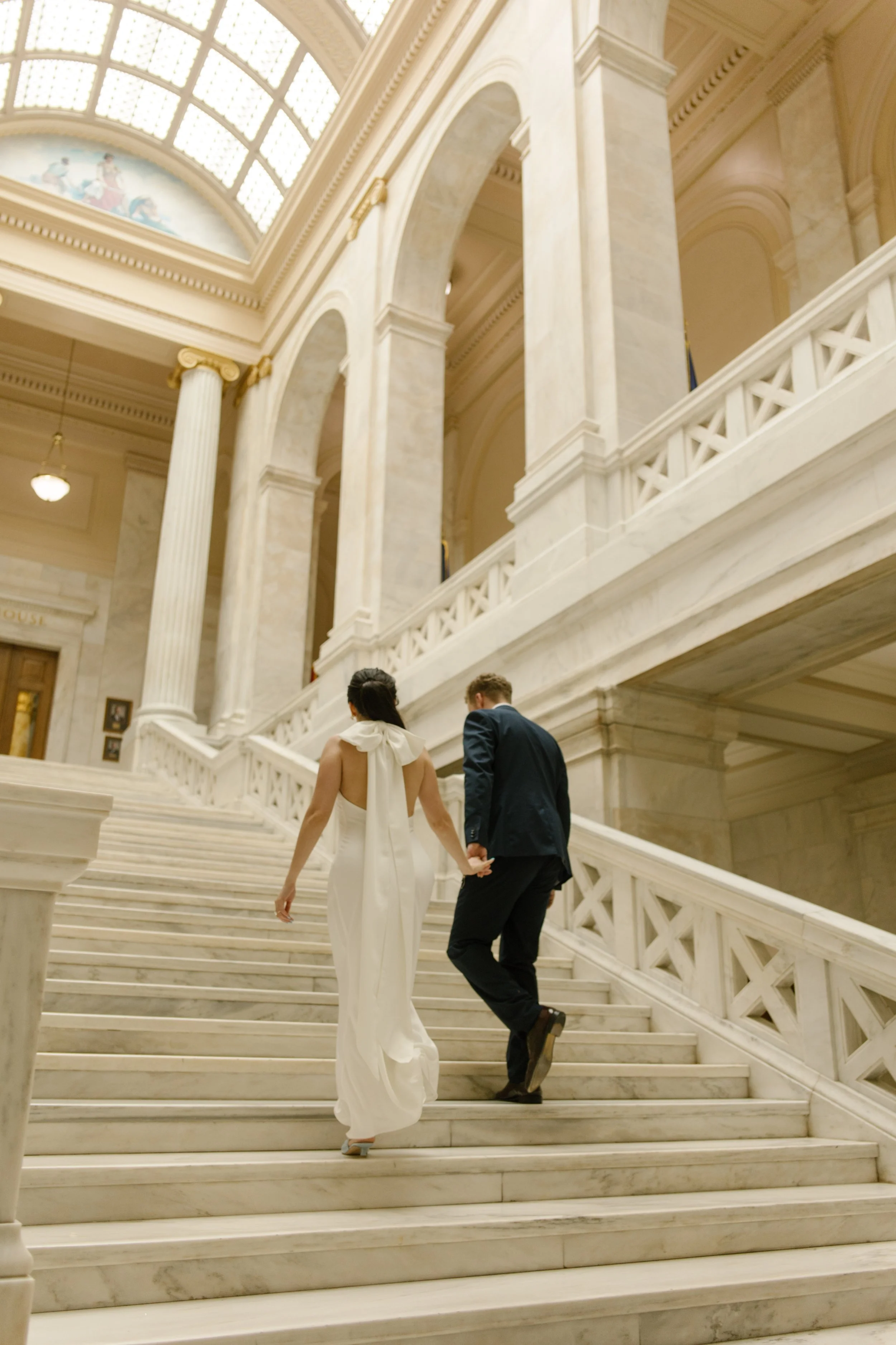 Newlywed couple walks hand in hand up the elegant marble stairs of the Little Rock courthouse.
