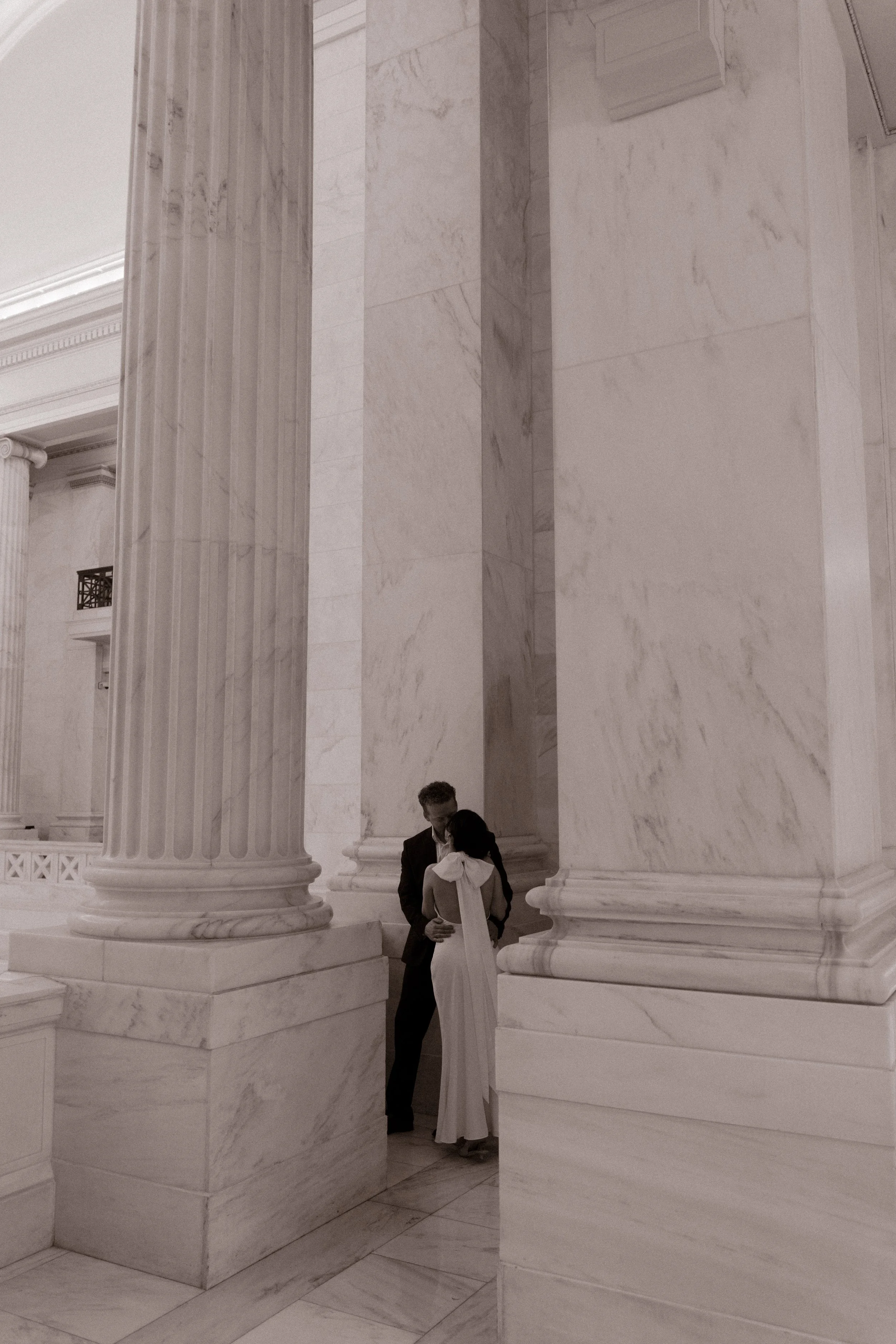 Couple sharing a quiet embrace between marble columns at the Little Rock Courthouse