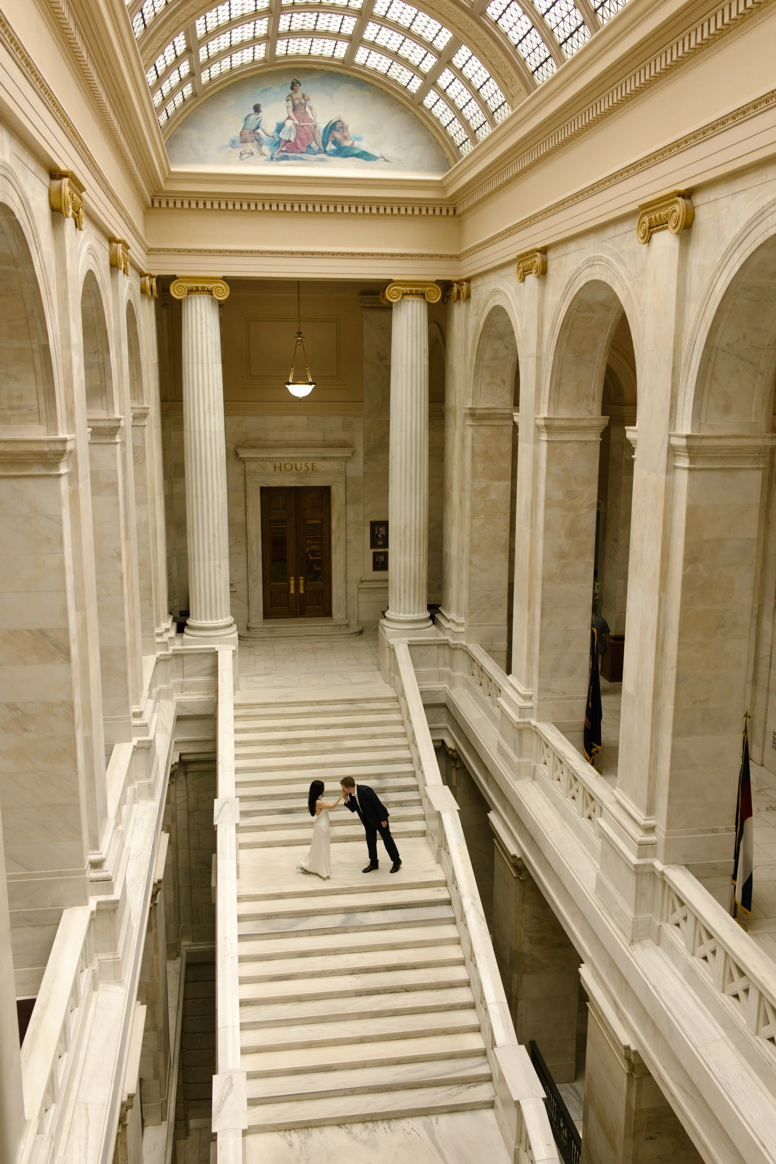 Wide architectural portrait of a couple sharing a kiss on the sweeping staircase inside the Little Rock courthouse.